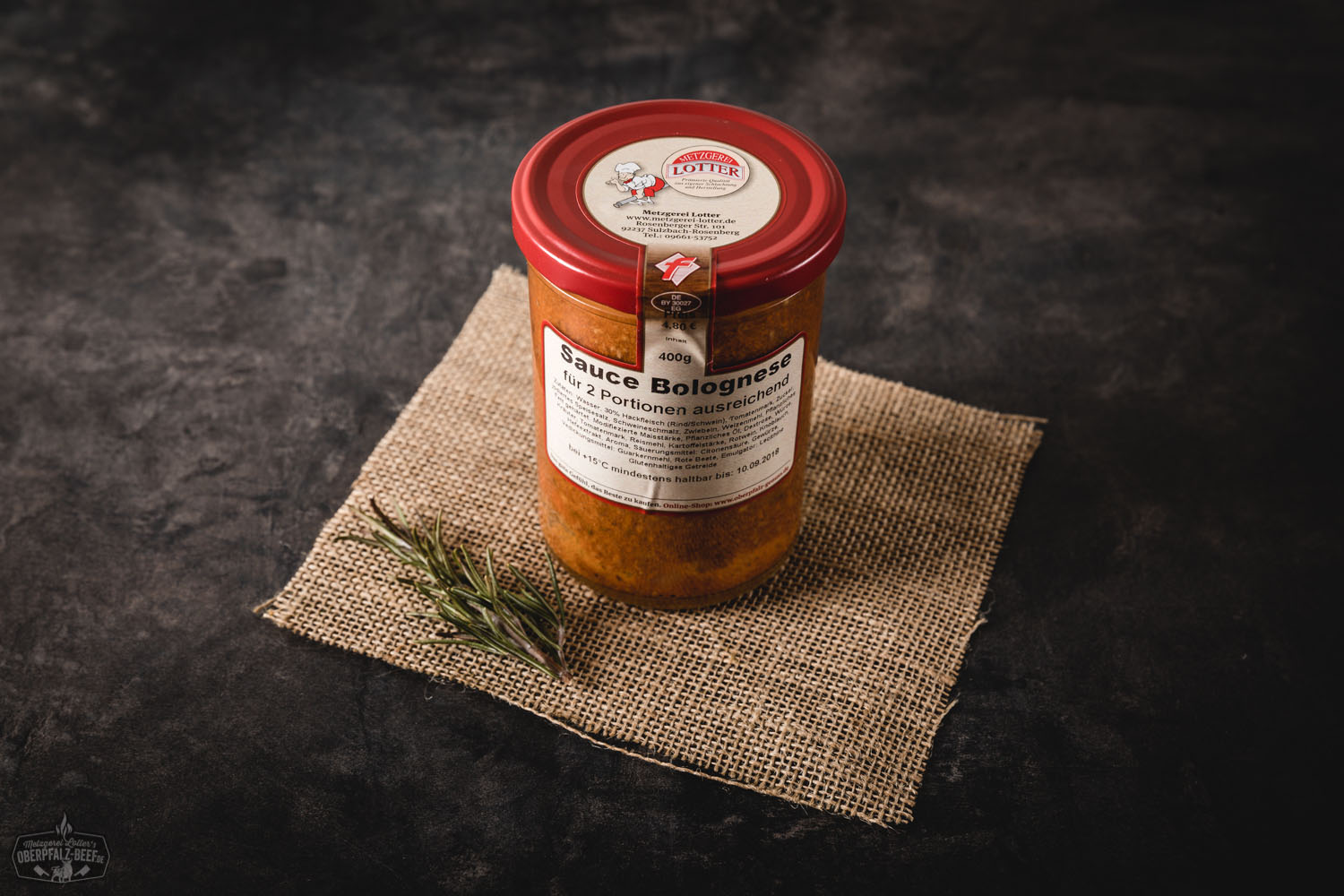Sauce Bolognese im Glas – Hausgemachte Fleischsoße aus Rindfleisch Ein Glas mit hausgemachter Sauce Bolognese, gefüllt mit stückiger Tomatensauce und sichtbaren Kräutern, steht auf einem dunklen Untergrund; im Hintergrund liegen rohe Spaghetti und Knoblauch – ideal für italienische Pasta-Rezepte.