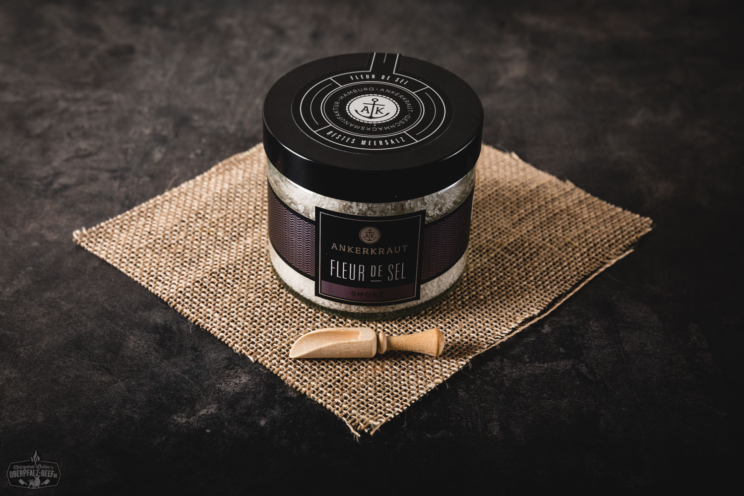Rundes Glas mit schwarzem Schraubdeckel, gefüllt mit geräuchertem Fleur de Sel der Marke Ankerkraut; das Etikett zeigt das Ankerkraut-Logo, Produktname „Fleur de Sel Smoke“ und dezente Holzoptik im Hintergrund – Gourmet-Gewürz für BBQ und Feinkost.