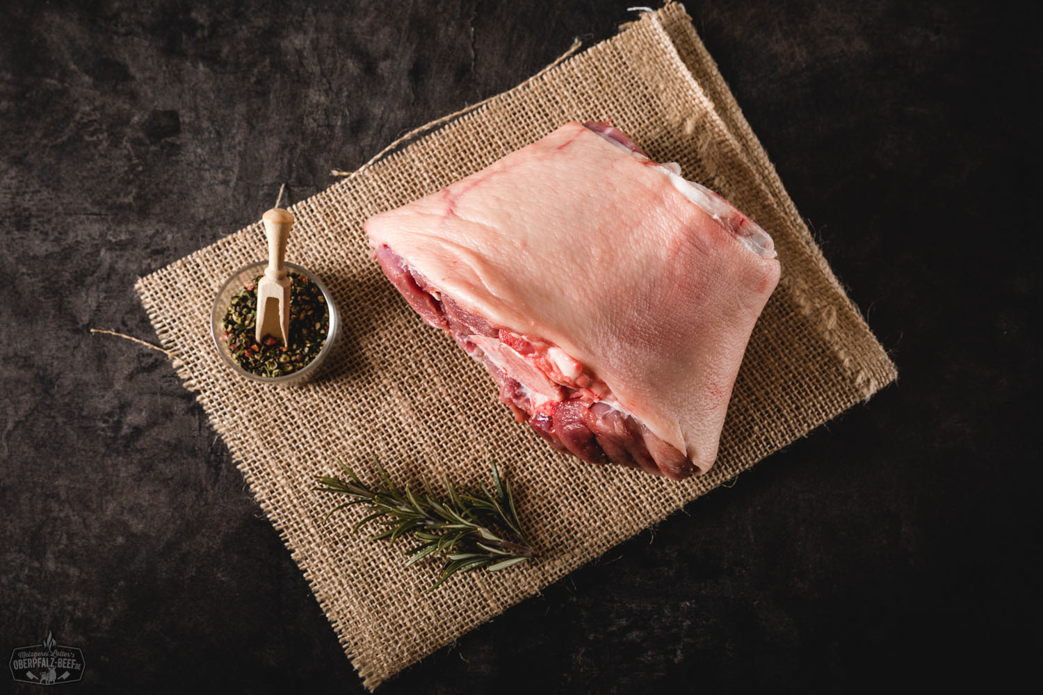 Vordere Haxe vom Oberpfälzer Landschwein – regionales Qualitätsschweinefleisch Rohes Stück Vordere Haxe vom Oberpfälzer Landschwein auf einem Holzbrett, umgeben von frischen Kräutern, Knoblauch und Pfefferkörnern – rustikale Fleischzubereitung in höchster Qualität.