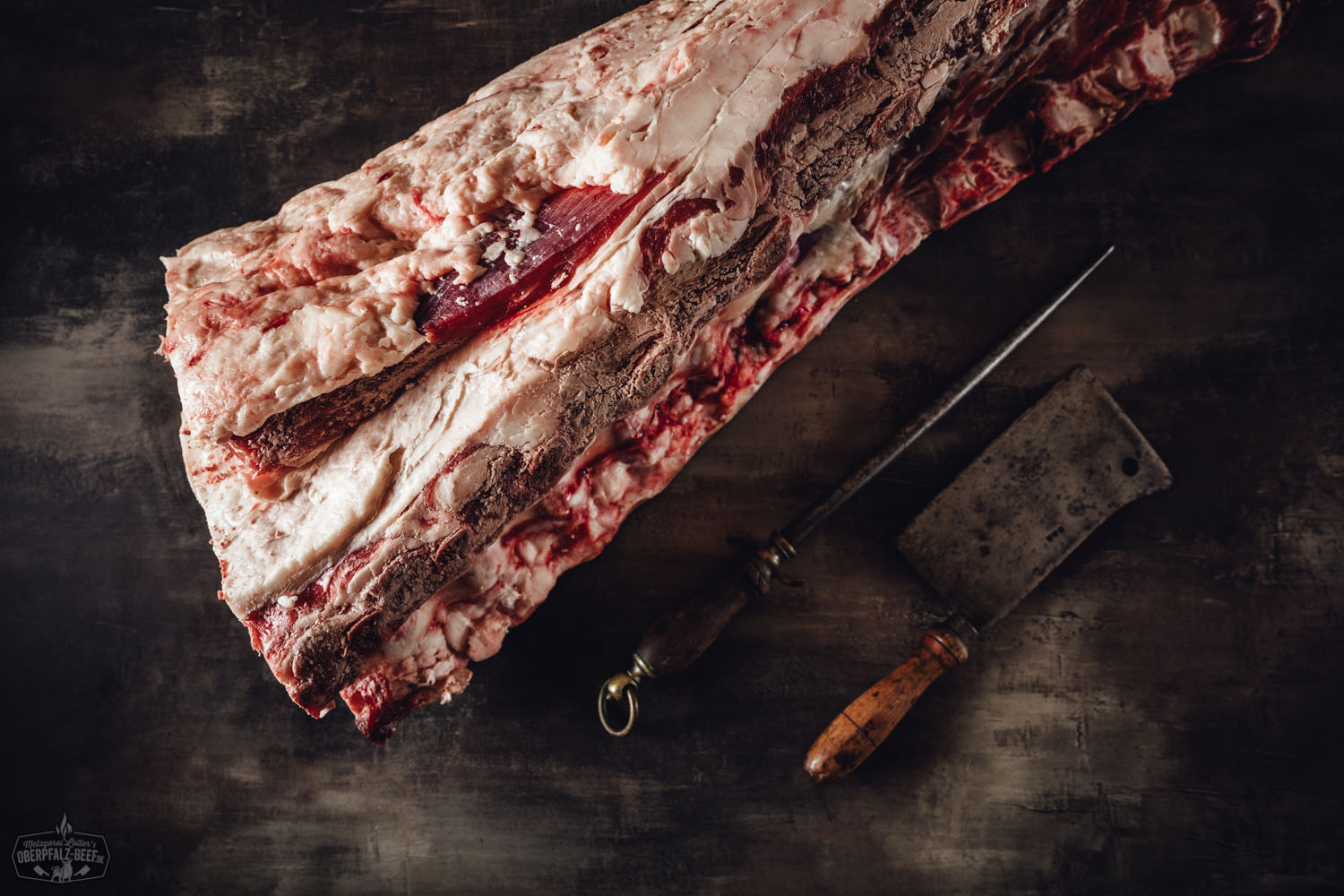 Ganzer Rinderrücken mit Knochen ohne Filet – zum Selberreifen vom Oberpfalz-Rind Roher Rinderrücken mit Knochen ohne Filet vom Oberpfalz-Rind, aufgeschnitten und bereit zum Selbstreifen; frisches Fleischstück mit sichtbarer Marmorierung auf hellem Untergrund, ideal für Dry Aged Beef.
