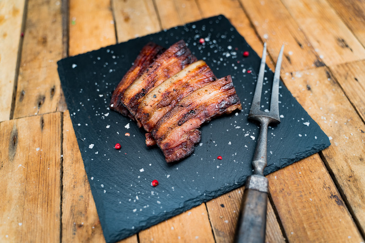 BBQ Bacon geschnitten vom Oberpfälzer Landschwein – Regionaler Genuss vom Grill Geschnittener BBQ-Bacon vom Oberpfälzer Landschwein, goldbraun gegrillt mit sichtbarer Fettmarmorierung, angerichtet auf dunklem Holzbrett, rustikales BBQ-Ambiente mit frischen Kräutern und Grillgewürzen im Hintergrund.