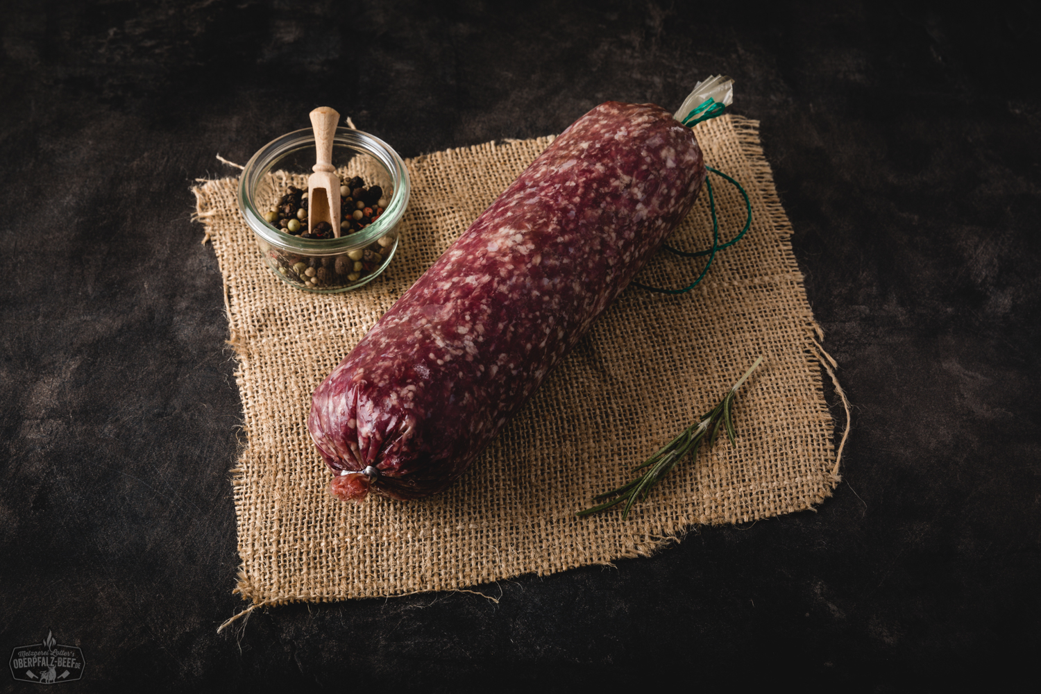 Frisch gemischtes Hackfleisch vom Oberpfälzer Rind und Schwein, roh und saftig, locker auf einem dunklen Holzbrett angerichtet, dekoriert mit Rosmarinzweig, grobem Salz und Pfefferkörnern – hochwertige regionale Fleischspezialität aus Bayern.