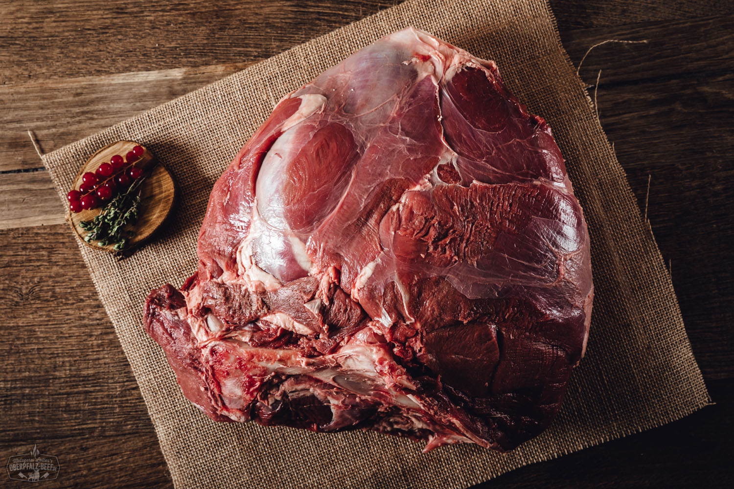 Frisch zerlegte Hirschkeule mit Knochen aus der Oberpfalz, roh und fettarm, auf dunklem Schiefer angerichtet – hochwertiges Wildbret mit sichtbarer Fleischstruktur und feiner Marmorierung für Wildliebhaber.