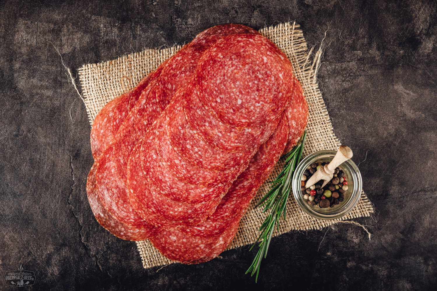 Geschnittene Fenchel-Chili-Salami auf Holzbrett – pikante Wurstspezialität Geschnittene Scheiben von zartem, rosafarbenem Kräuterschinken auf einem Holzbrett angerichtet, dekoriert mit frischen Kräutern wie Rosmarin und Petersilie, vor hellem, neutralem Hintergrund – delikate Fleischspezialität aus der Oberpfalz.