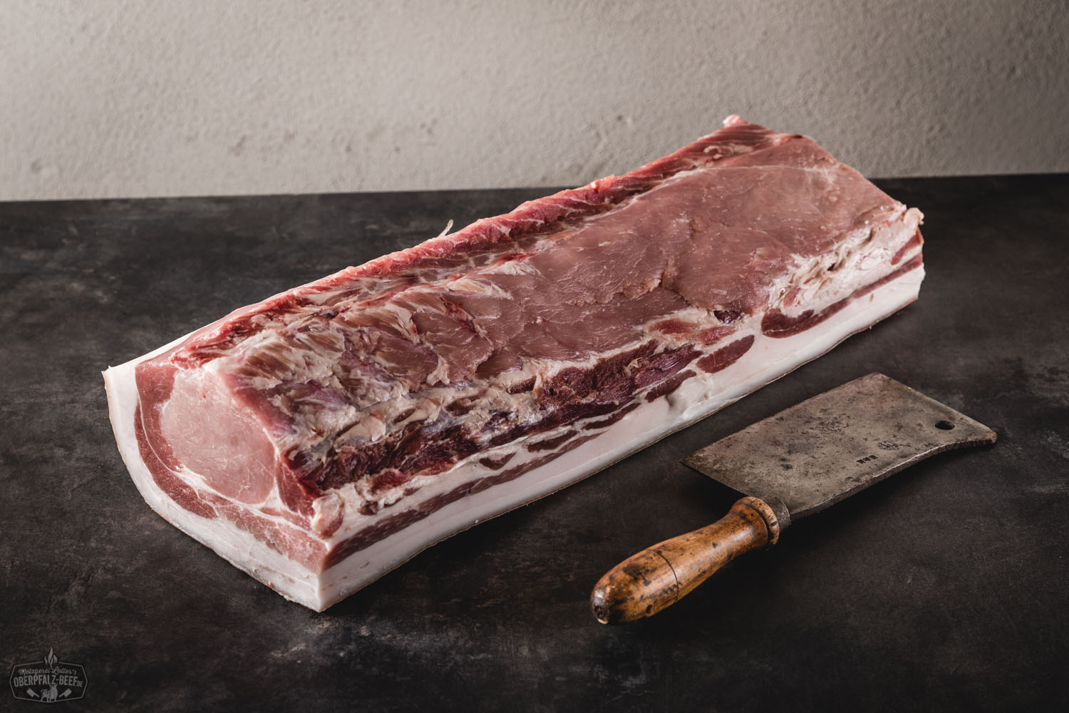Dry Aged Kotelett mit Schwarte vom Oberpfälzer Landschwein – regionales Premiumfleisch Ganzes Dry-Aged Kotelett mit Schwarte vom Oberpfälzer Landschwein, roh auf dunklem Untergrund präsentiert, marmoriertes Fleisch mit ausgeprägtem Fettrand – hochwertiges Stück Fleisch für Grill oder Ofen.