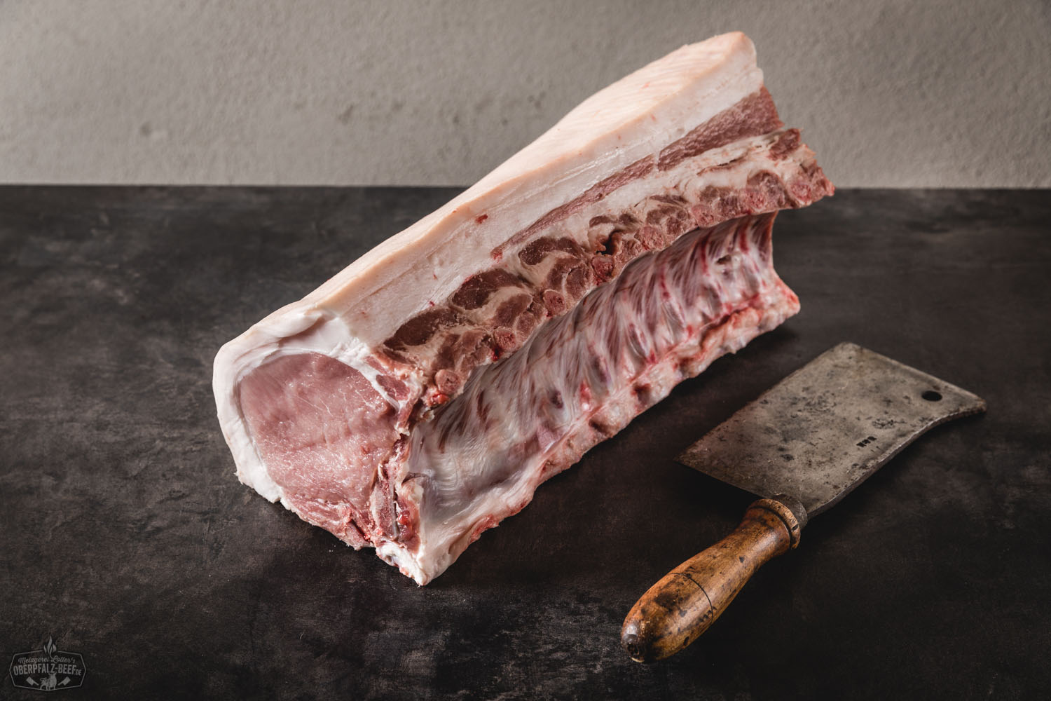 Halbes Kotelett Classic Cut vom Oberpfälzer Landschwein – Frisch aus artgerechter Haltung Frisches halbes Kotelett vom Oberpfälzer Landschwein im Classic Cut, roh auf schwarzem Untergrund präsentiert, mit sichtbarer Marmorierung und Fettrand – hochwertiges Schweinefleisch für Grill oder Pfanne.
