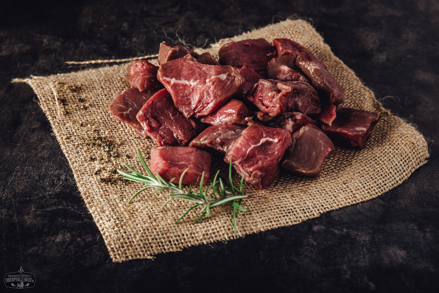 Handgeschnittene Fondue-Fleischstücke aus Rinderhüfte, roh und gleichmäßig geschnitten, frisch angerichtet auf einem dunklen Teller mit feiner Marmorierung, ideal für Fondue oder Raclette – hochwertiges Rindfleisch aus der Oberpfalz.