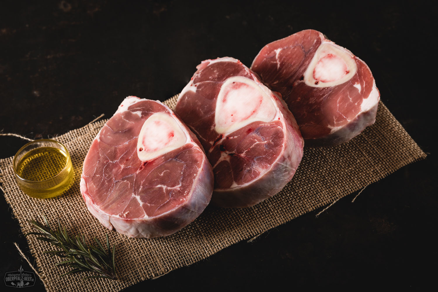 Ossobuco vom Oberpfälzer Milchkalb auf einem rustikalen Holzbrett angerichtet, begleitet von frischen Kräutern und Gemüse.