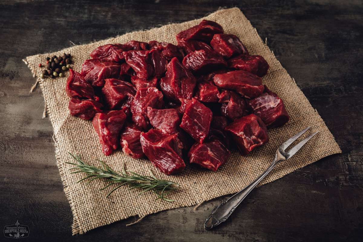 Handgeschnittenes Gulasch vom Oberpfalz-Rind – Frisch & Regional Rinderbraten aus der falschen Lende vom Oberpfalz-Rind, roh und mariniert, auf schwarzem Untergrund angerichtet, mit frischen Kräutern und Gewürzen garniert – hochwertiges deutsches Rindfleisch ideal zum Schmoren oder Braten.