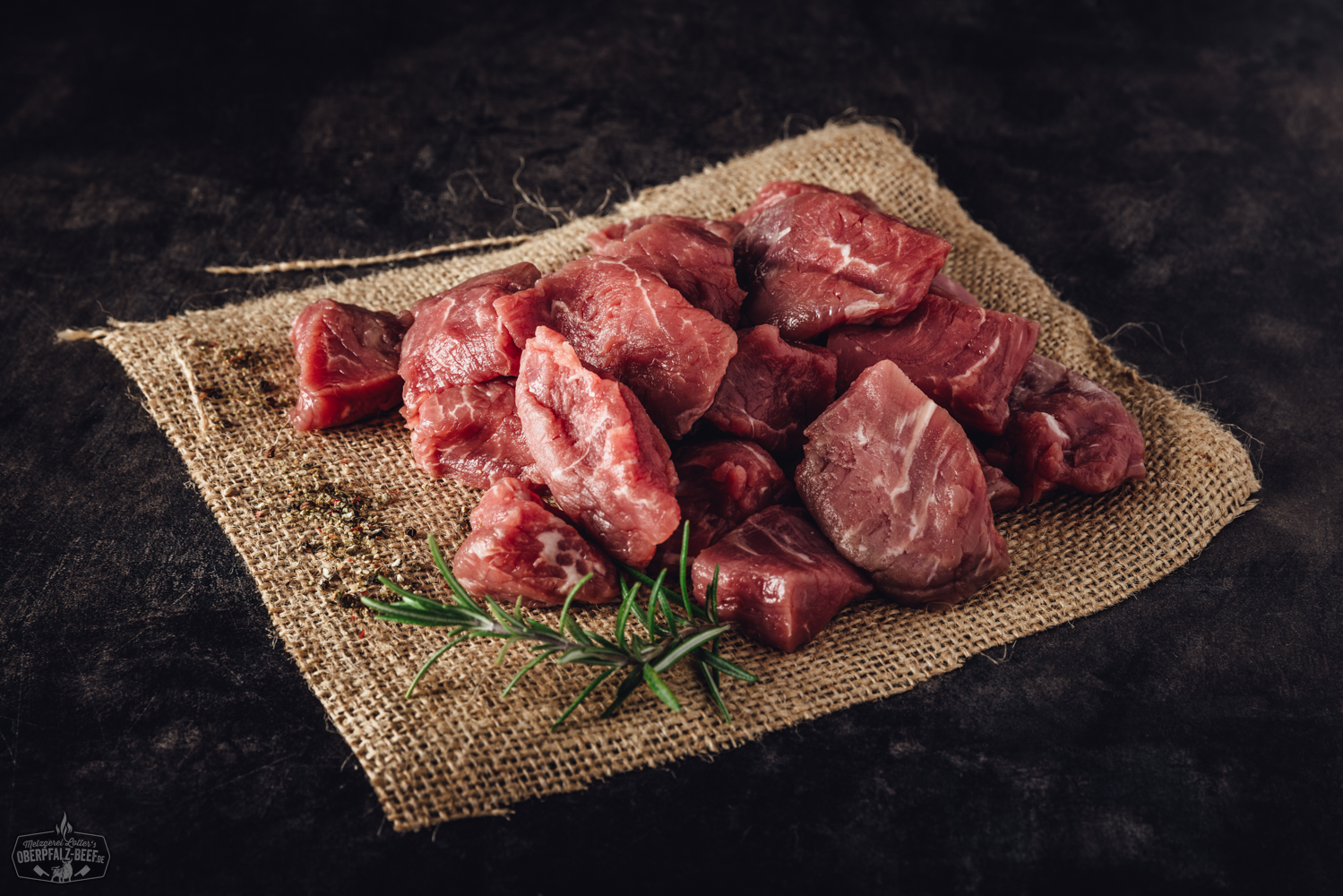 Handgeschnittenes Rinderfilet für Fondue – Premium Beef aus der Oberpfalz Handgeschnittenes Rinderfilet-Fonduefleisch roh auf einem Holzbrett angerichtet, umgeben von frischen Kräutern, rosa Pfefferkörnern und grobem Meersalz – hochwertige Zubereitung für Fondue oder Grillgerichte.