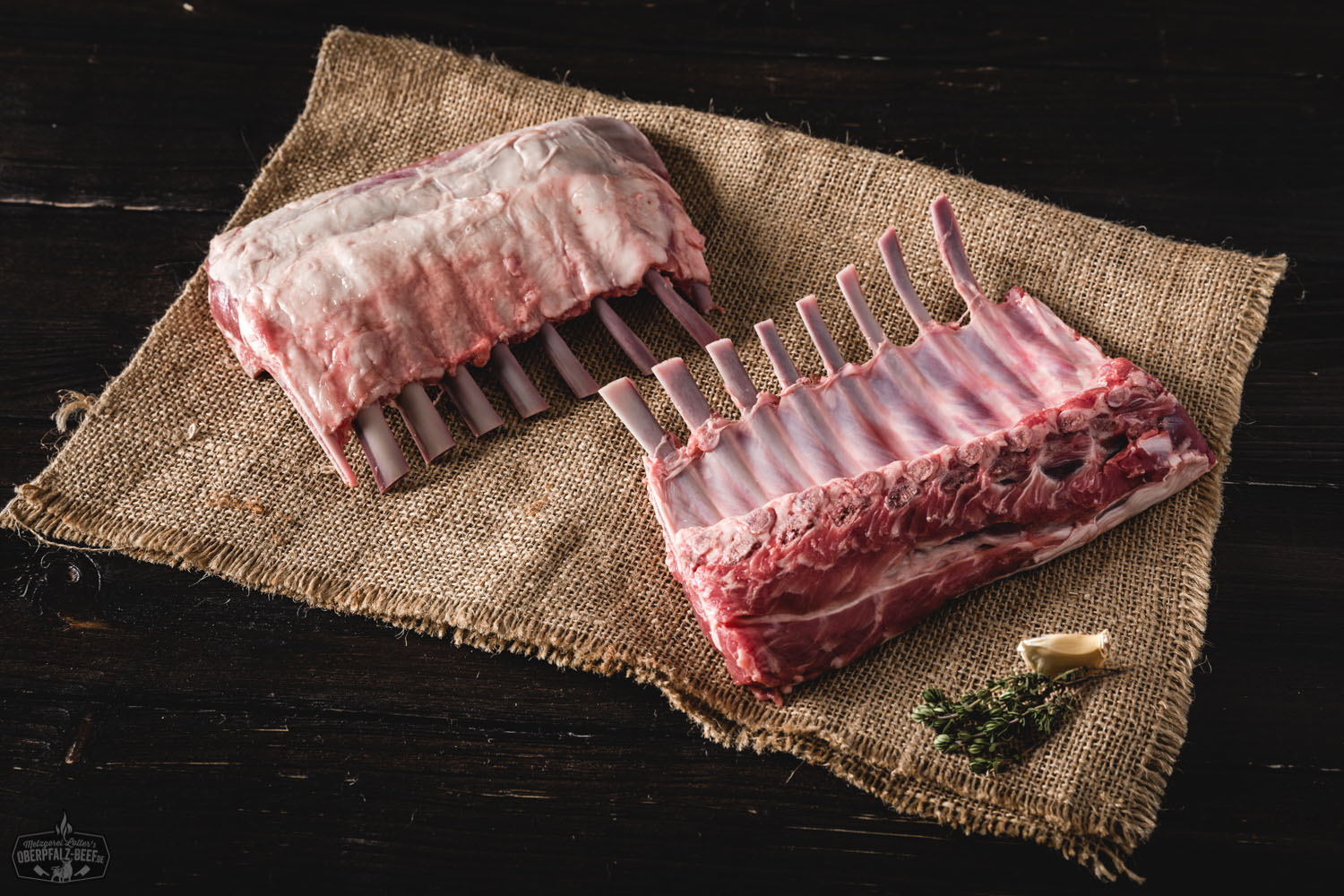 Hochwertige Lammracks vom Juradistl Lamm mit frischen Kräutern und Gewürzen, saftig und zart gegrillt, auf einem rustikalen Holzbrett präsentiert. Perfect für Feinschmecker und Liebhaber von regional erzeugtem Fleisch.