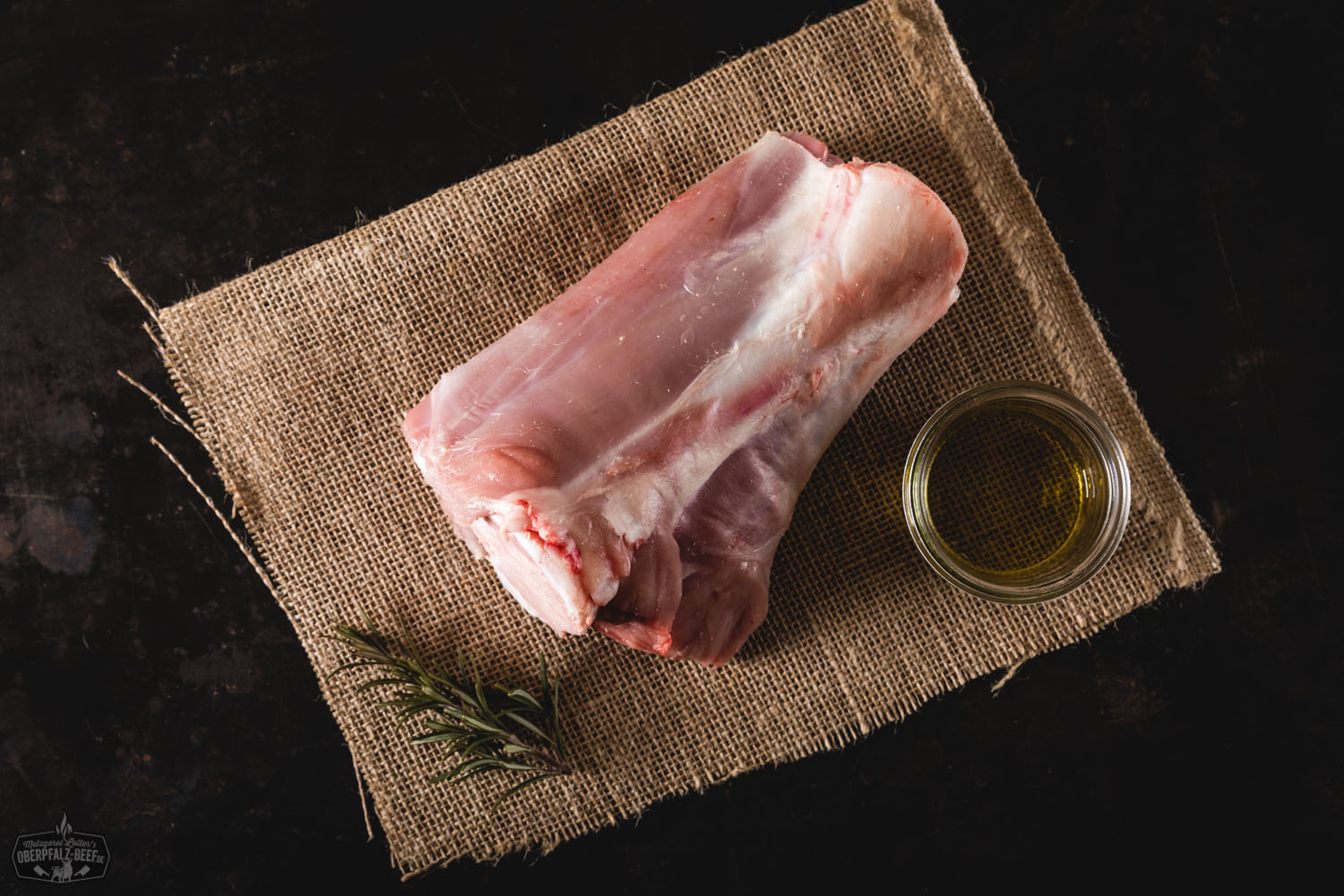 Hintere Haxe vom Oberpfälzer Milchkalb – zartes Kalbfleisch aus regionaler Aufzucht Rohe hintere Kalbshaxe vom Oberpfälzer Milchkalb auf dunkler Schieferplatte, umgeben von Rosmarinzweigen, Knoblauchzehen, Meersalz und buntem Pfeffer – hochwertiges Kalbfleisch für Schmorgerichte, Metzgerqualität aus der Oberpfalz.