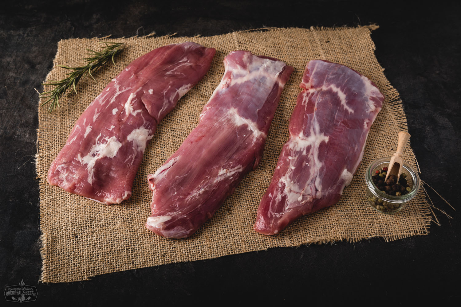 Perfekt medium gebratenes Flanksteak vom Oberpfälzer Landschwein auf Holzbrett serviert, saftig aufgeschnitten mit sichtbarer Maserung und zartem Fleisch, umgeben von frischen Kräutern und rustikalem Ambiente – hochwertiges Schweinefleisch aus Bayern.