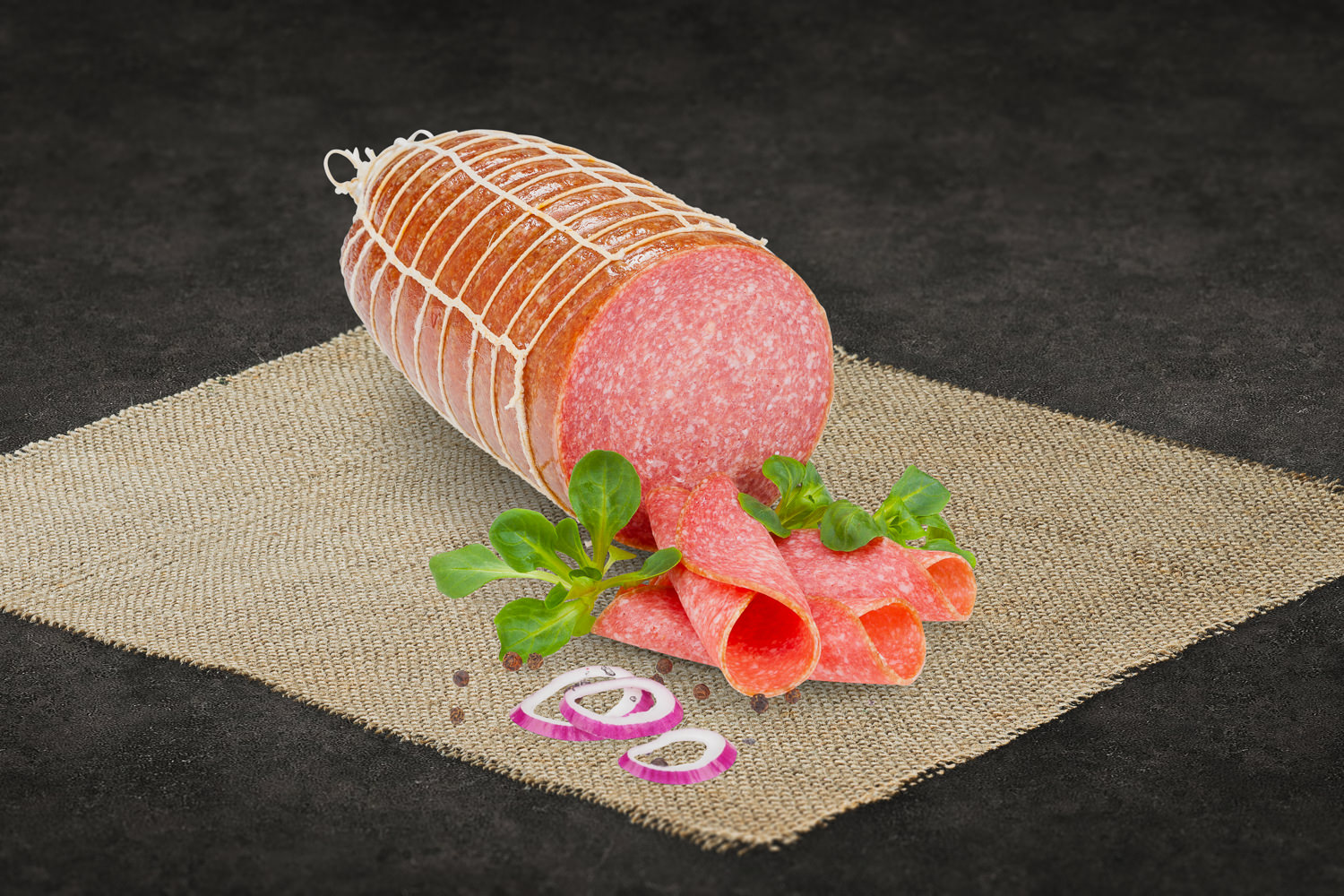 Mehrere Scheiben geschnittene Pizzasalami mit sichtbarer grober Körnung, rötlich-brauner Farbe und leicht glänzender Oberfläche, auf einem neutralen Untergrund angerichtet – ideal für Pizza oder Brotbelag.