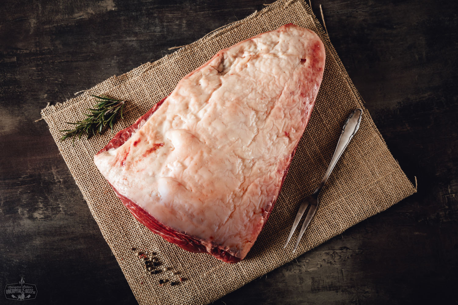 Picanha Wet Aged vom Oberpfalz-Rind – Premium Rindfleisch kaufen Rohes Picanha-Steak vom Oberpfalz-Rind liegt auf einem dunklen Holzbrett, umgeben von grobem Meersalz, frischen Kräutern und Knoblauch; hochwertiges Wet Aged Beef mit deutlicher Marmorierung – ideale Fleischqualität für Steakliebhaber.