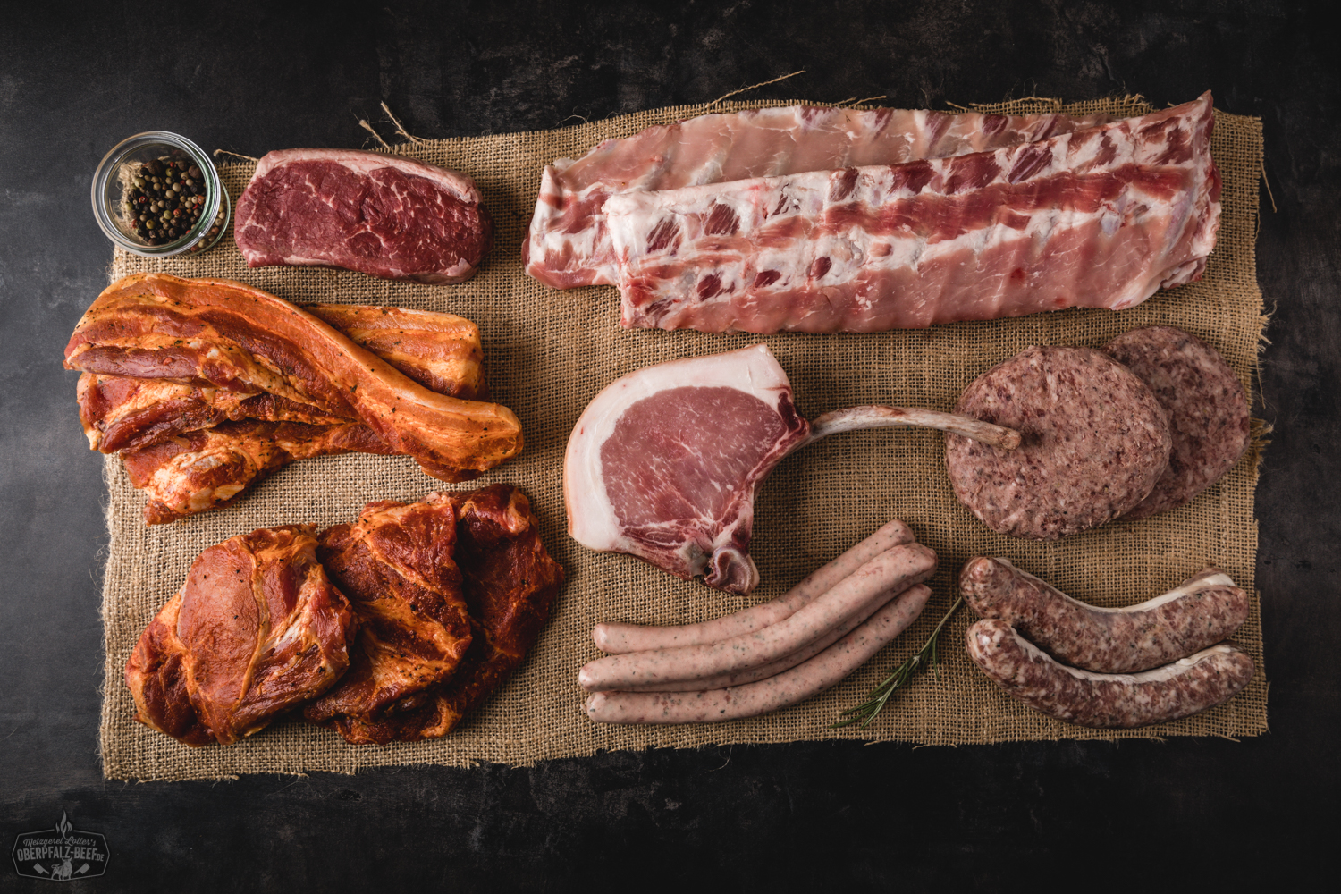 Grillpaket Special mit hochwertigem Oberpfalz-Beef – Frisches Premium-Fleisch für echten Grillgenuss Grillpaket mit hochwertigem Oberpfalz-Beef: Verschiedene Stücke marmoriertes Rindfleisch appetitlich auf Holzuntergrund angerichtet, darunter Tomahawk-Steak, Rumpsteak, Rib-Eye und Würstchen; ideal für Grillfreunde und BBQ-Liebhaber.