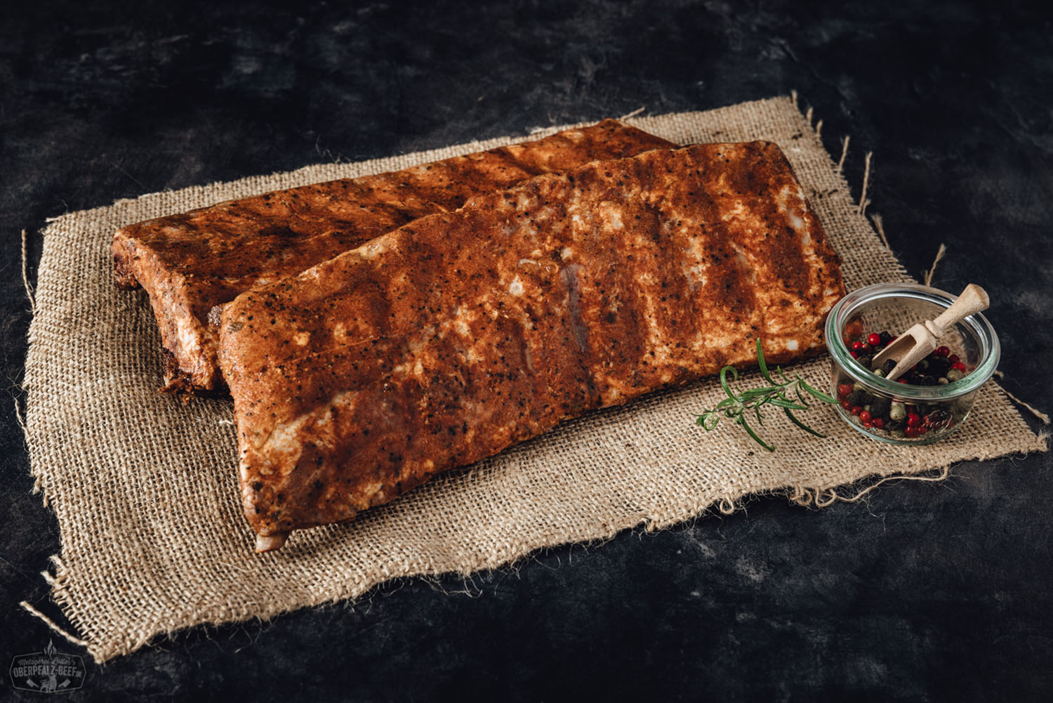 Sous-vide gegarte Baby Back Ribs vom Oberpfälzer Landschwein – zart & BBQ-ready Sous-vide gegarte Baby Back Ribs vom Oberpfälzer Landschwein, knusprig glasiert und serviert auf einem Holzbrett mit frischen Kräutern und Barbecue-Sauce – zartes Fleisch mit rauchiger Note, perfekt zubereitet für BBQ-Liebhaber.
