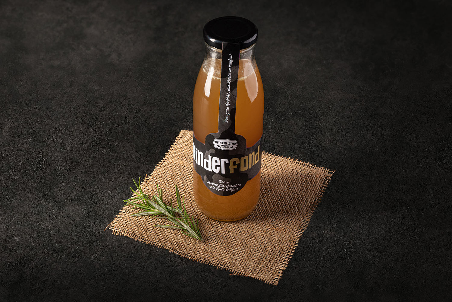 Ein Glas mit dunkelbraunem, klarem Rinderfond auf Holzuntergrund, daneben frische Zutaten wie Karotten, Sellerie und Lauch, symbolisieren hausgemachten Rinderfond aus natürlichen Zutaten.