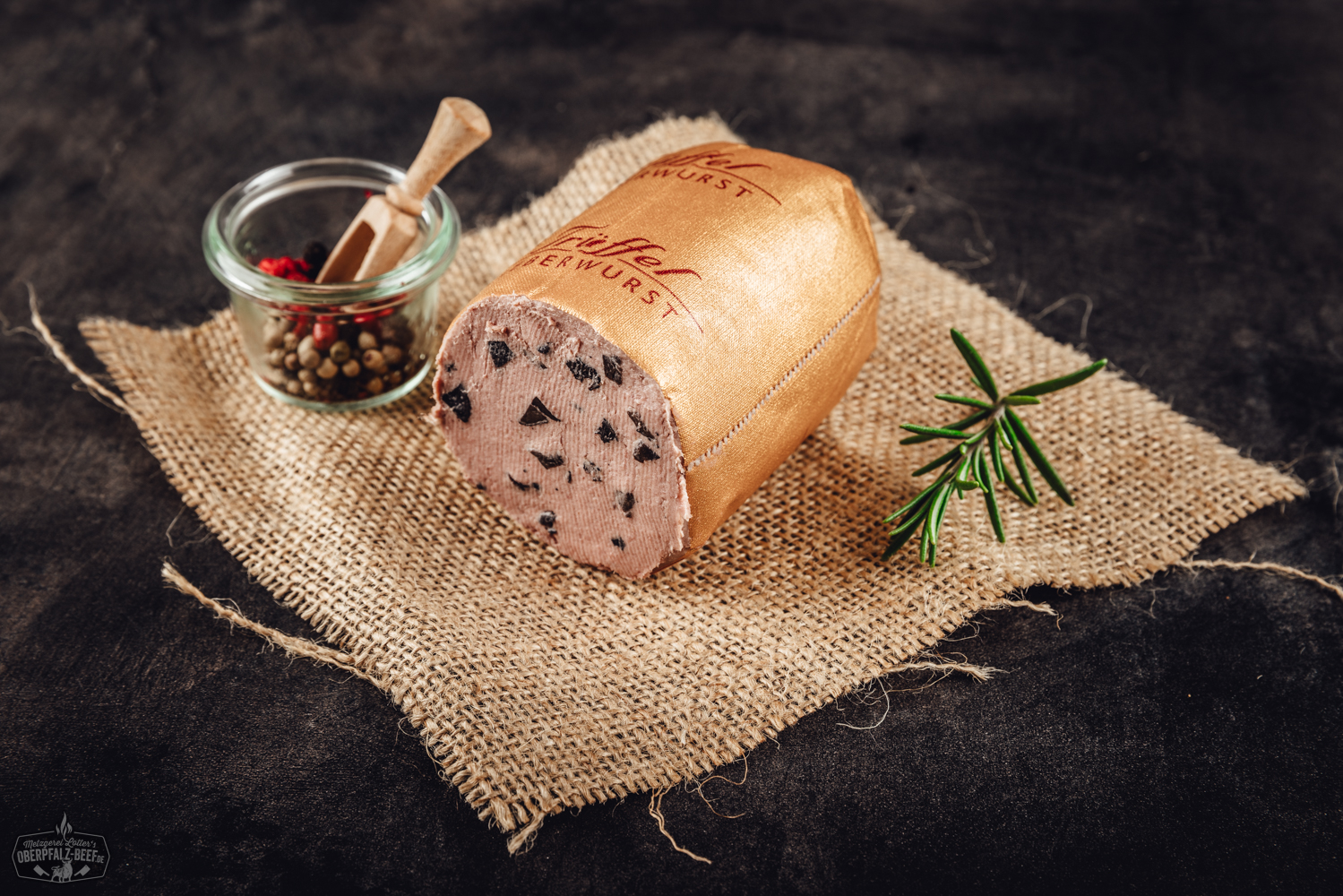 Trüffel-Kalbfleisch-Leberwurst im Glas – Feinkost aus der Oberpfalz Nikolaus-Salami in Portionsgröße mit roter Weihnachtsverpackung, weißem Nikolaus-Motiv und goldener Aufschrift „Nikolaus Salami“; dekorativ arrangiert auf Holztisch mit Tannenzweigen – festliche Wurst-Spezialität aus der Oberpfalz.