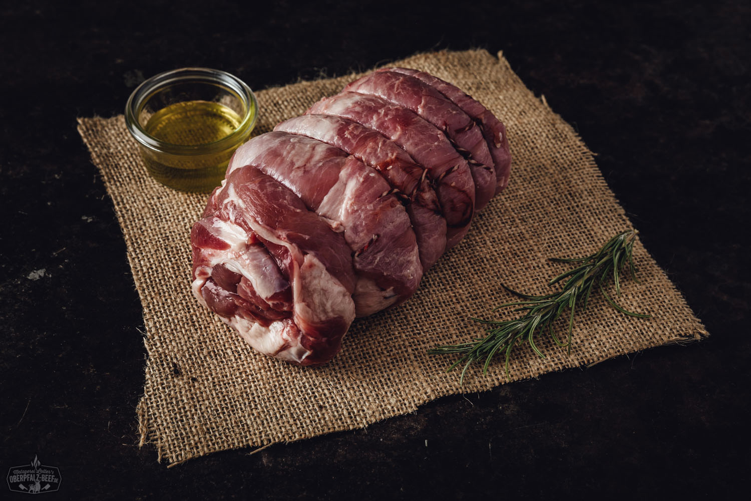 Kalbsrollbraten mit extra magerem Kern, aufgeschnitten auf einem dunklen Holzbrett angerichtet, sichtbar saftig und zart, begleitet von Kräutern und Gewürzen – perfekt gegartes Fleischgericht für Genießer.