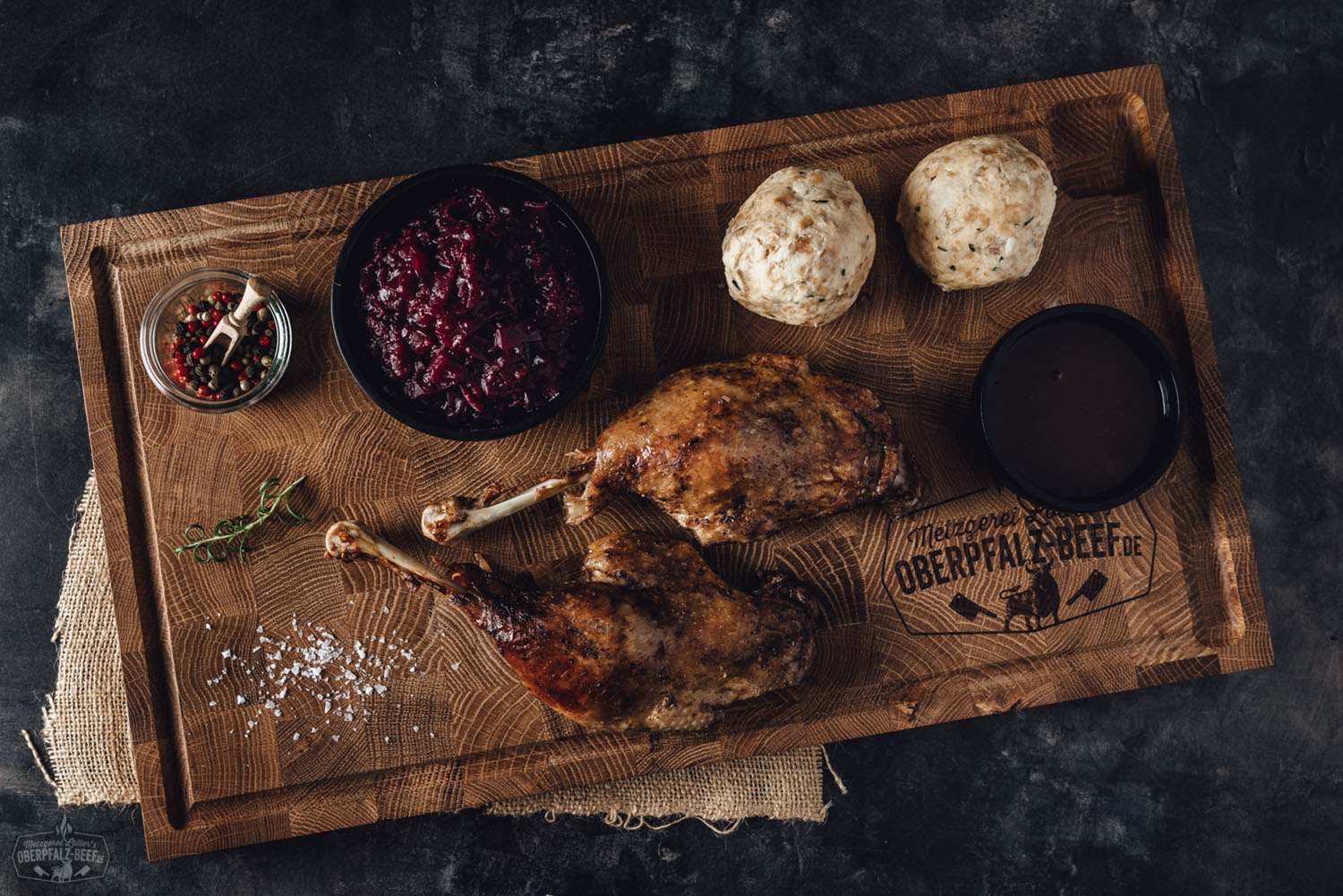 Oberpfälzer Gänsebox mit knuspriger Gänsekeule und Beilagen – Festessen online bestellen Zubereitete Gänsekeule mit knuspriger Haut auf einer rustikalen Holzplatte, serviert mit Kartoffelknödeln, Blaukraut und einer dunklen Bratensoße – traditionelle Oberpfälzer Spezialität festlich angerichtet.