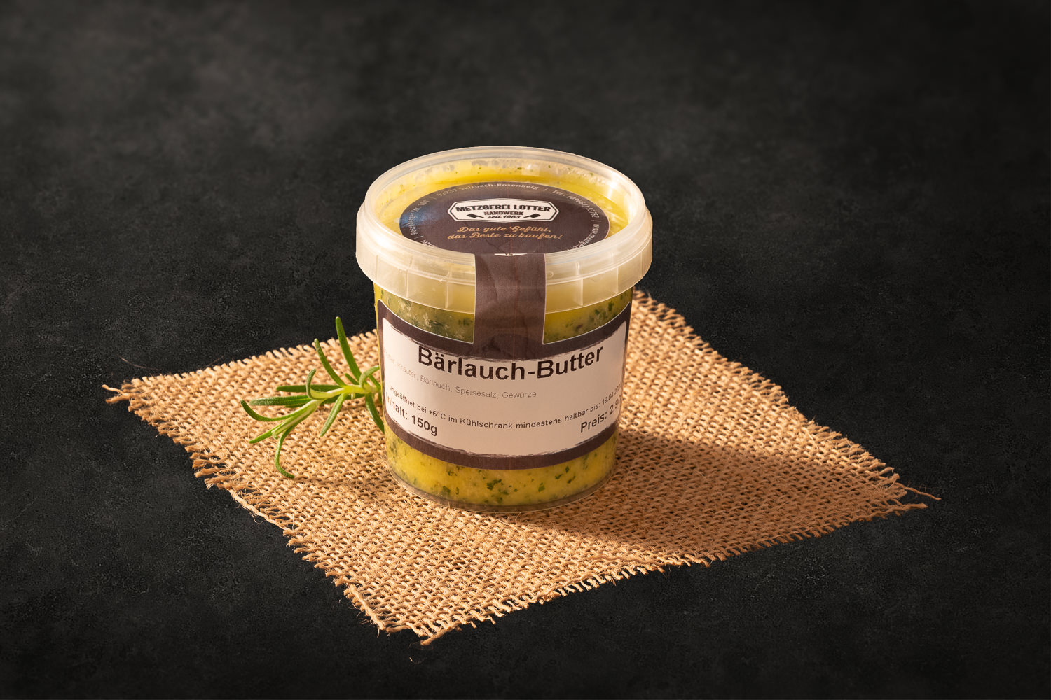 Hausgemachte Bärlauchbutter in weißer Schale, angerichtet auf einem dunklen Holzbrett mit frischen Bärlauchblättern, Meersalz und Butterstücken – rustikale Präsentation für Grillbeilage oder Brotaufstrich.