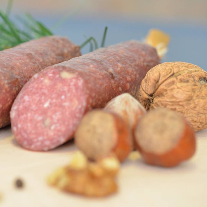 Mandel Amaretto Salami – Feinkost-Salami mit Mandeln und Amaretto-Aroma Nahaufnahme einer Mandel-Amaretto-Salami auf dunklem Untergrund; die aufgeschnittene Salami zeigt eine grobkörnige Struktur mit sichtbaren Mandelstücken, daneben liegen ganze Mandeln und ein Amarettokeks – hochwertige Delikatesswurst mit edlem Aroma.