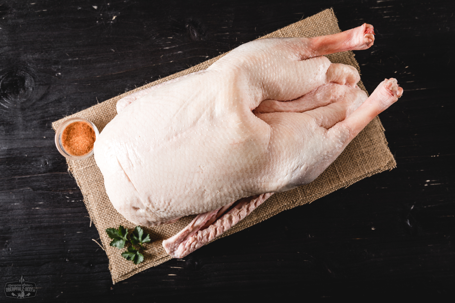 Knusprig gebratene Martinsgans mit goldbrauner Haut auf einem Holzbrett angerichtet, umgeben von Orangenscheiben, Maronen und frischen Kräutern; traditionelle Festtagsmahlzeit, perfekt für Weihnachten oder St. Martins Feier.