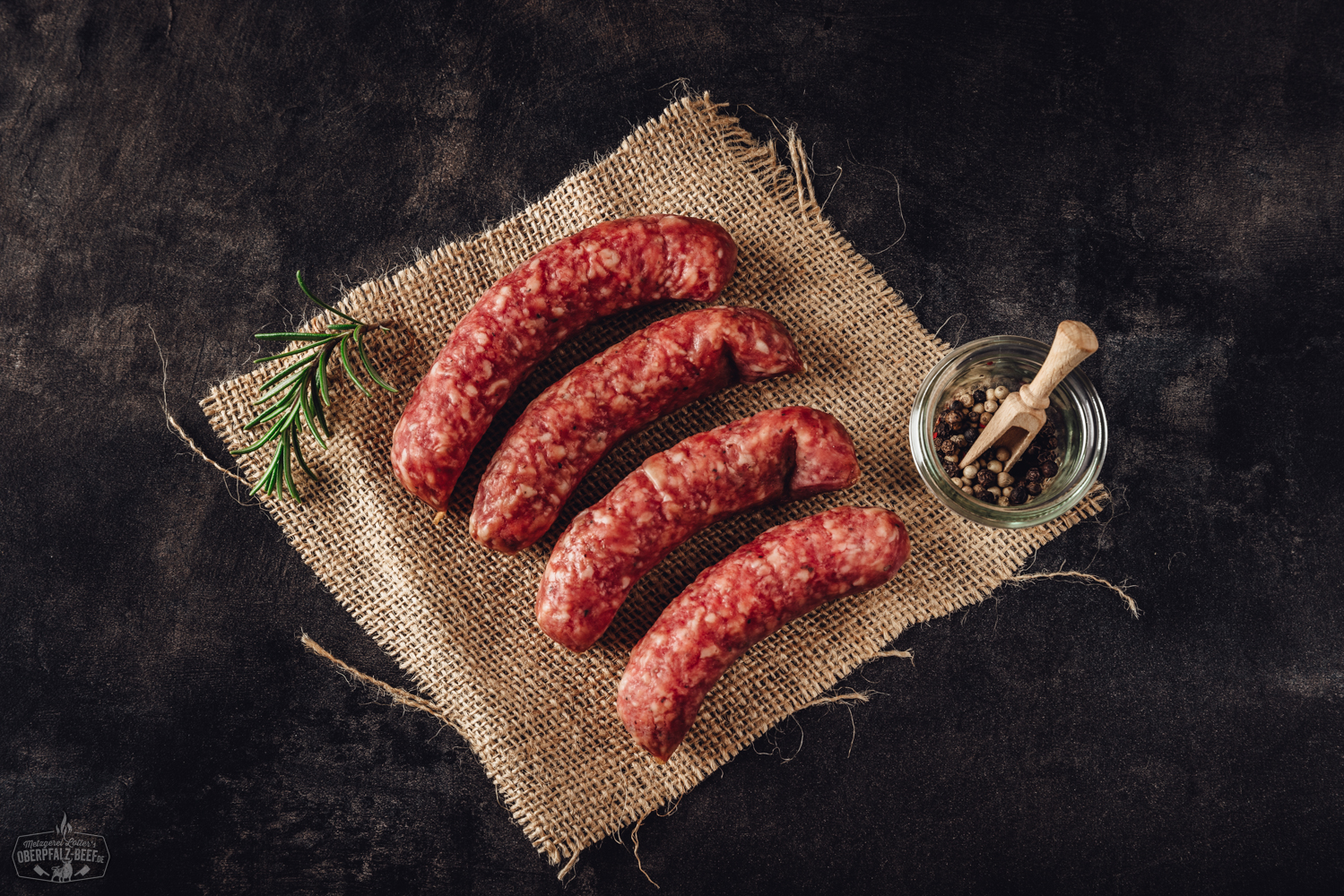 Mediterranos Grillplatte mit Rind, Gemüse und Rosmarin auf heißem Stein – Oberpfalz Beef Spezialität Weihnachtlich verpackte Salami in rotem Nikolausmantel mit weißem Bart und Mütze, stehend vor rustikalem Holz-Hintergrund, daneben Tannenzweige und Weihnachtsdekoration – festliche Wurst als Geschenkidee zu Weihnachten.