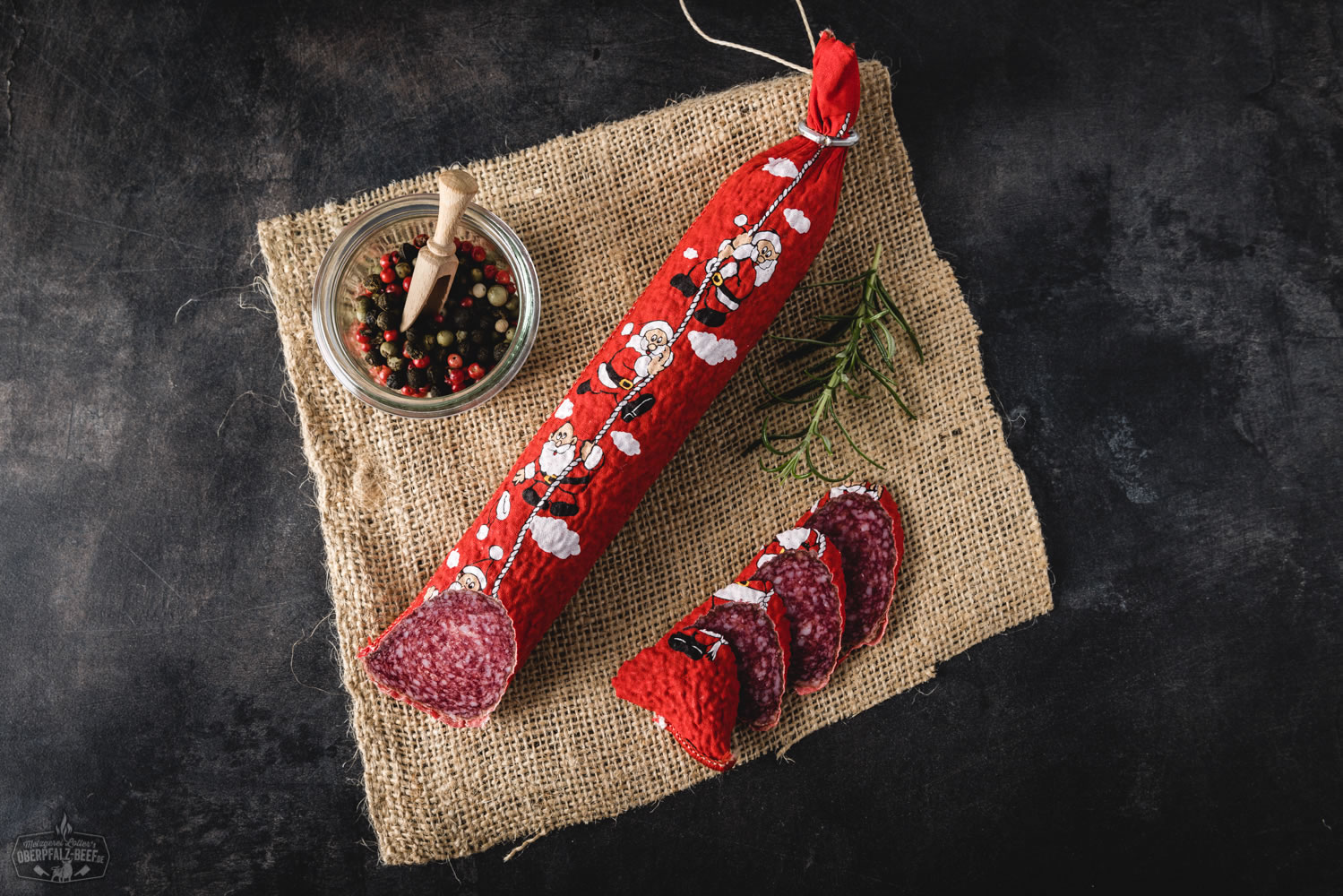 Nikolaus Salami am Seil – traditionelle Wurstspezialität aus der Oberpfalz Nikolaus-Salami am roten Band aufgehängt vor hellem Hintergrund, traditionelle Rohwurst in Geschenkform mit rotem Etikett und weihnachtlicher Aufschrift, ideale Delikatesse zu Weihnachten – Oberpfalz-Beef Spezialität.