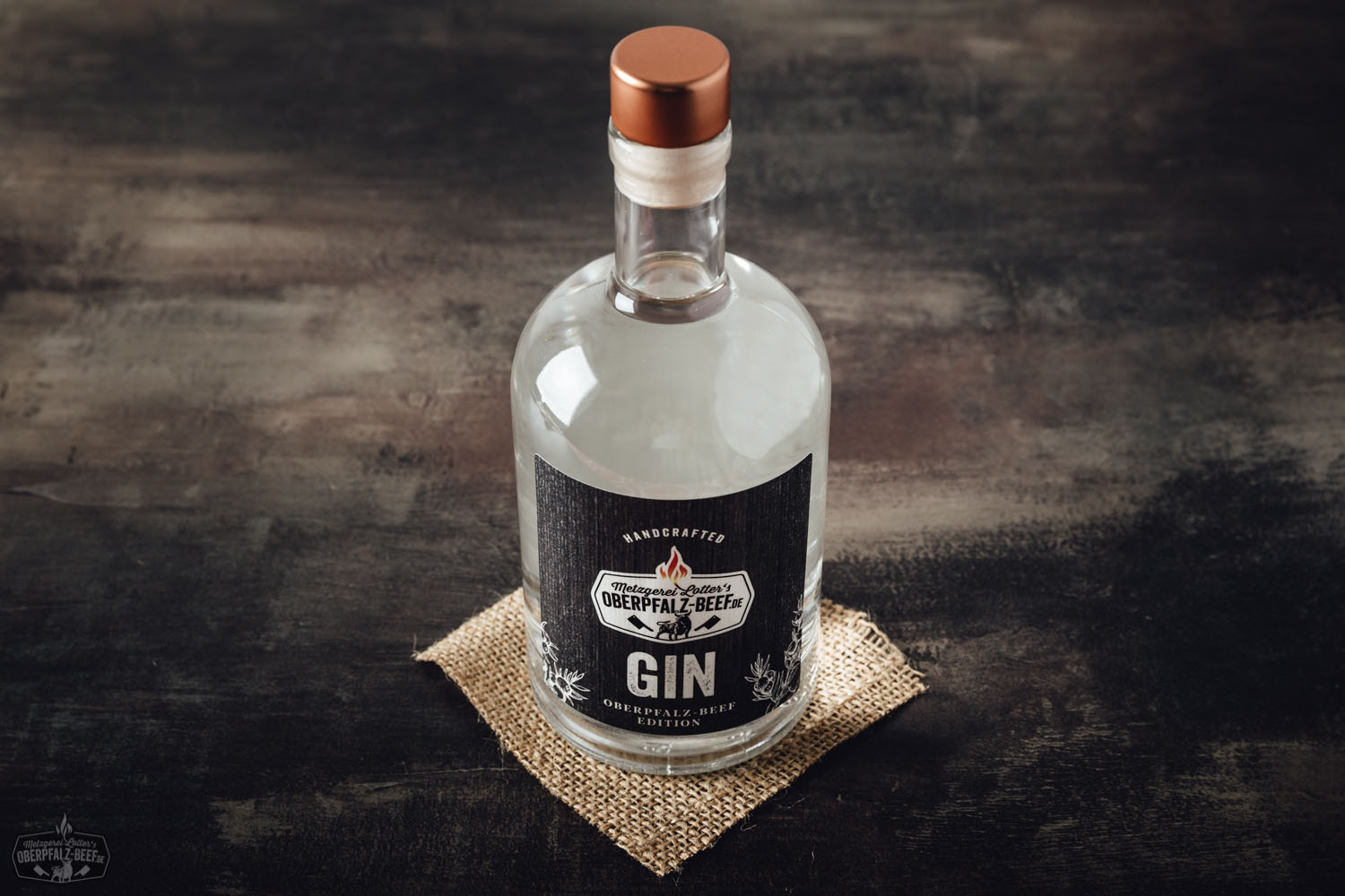 Handcrafted Oberpfalz Beef Gin – Regionaler Premium-Gin mit Rindfleischnote aus Bayern Flasche Handcrafted Oberpfalz Beef Gin auf rustikalem Holzuntergrund, flankiert von Wacholderbeeren, Kräutern und Zitrusfrüchten, stimmungsvoll arrangiert in natürlichem Licht – hochwertiger, regionaler Gin aus der Oberpfalz.