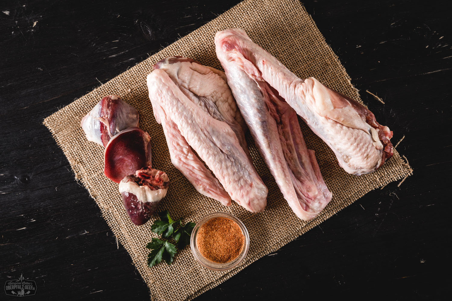 Frisches, rohes Gänsekleinfleisch von der Oberpfälzer Bauerngans auf einem rustikalen Holzbrett angerichtet, umgeben von Gewürzen, Kräutern und Gemüse, ideal zur Zubereitung von Suppen und Brühen – regionales Bio-Geflügel aus nachhaltiger Aufzucht.