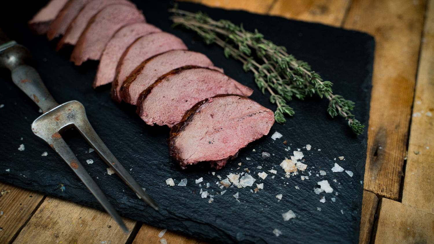 Rücken ohne Knochen vom Oberpfälzer Wildschwein – Frisches Wildfleisch regionaler Herkunft Frischer, roher Wildschweinrücken ohne Knochen aus der Oberpfalz, auf schwarzem Untergrund angerichtet, mit sichtbarer Marmorierung und frischem Rosmarinzweig garniert – hochwertiges Wildfleisch für Wildschwein-Rezepte und Fleischliebhaber.