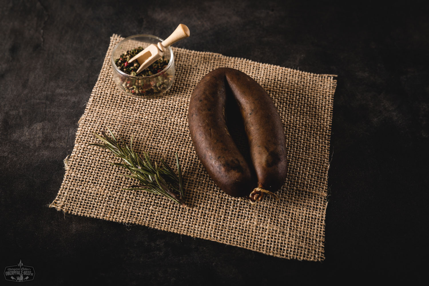 Oberpfälzer geräucherte Leberwurst im Ring – Regionales Fleischprodukt Ein geräucherter Ring Oberpfälzer Leberwurst auf einem rustikalen Holzbrett mit einem Messer, umgeben von frischen Kräutern und Gewürzen.