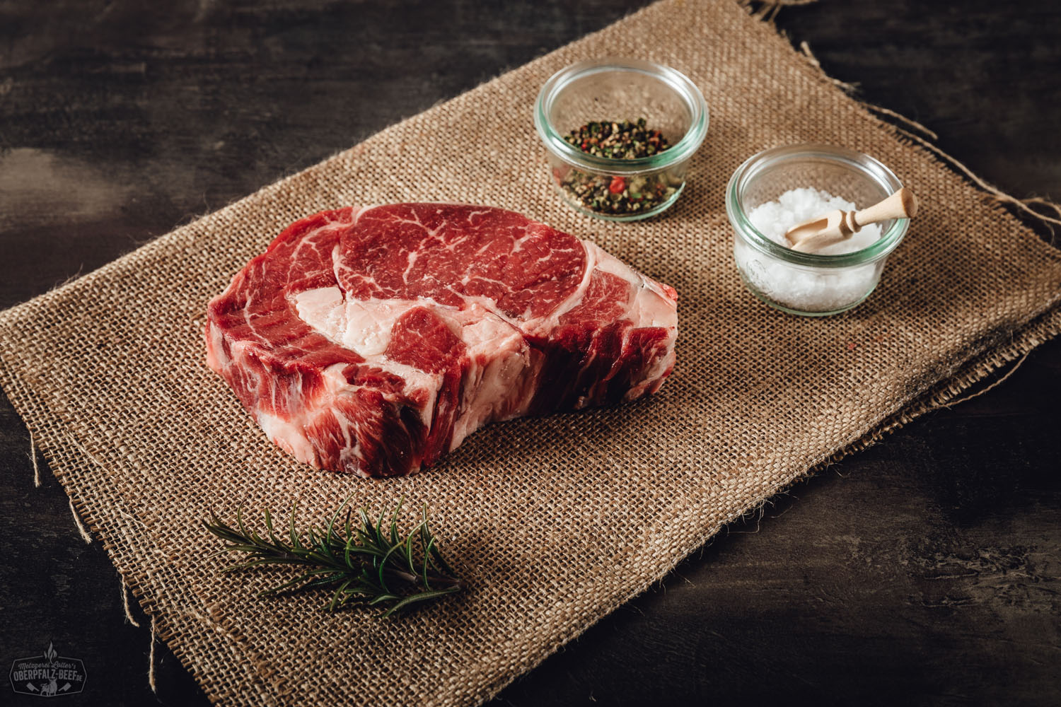 Nahaufnahme eines dry-aged Entrecôte-Steaks (Rib-Eye) vom Oberpfalz-Rind auf einem dunklen Untergrund, gut marmoriert mit sichtbarem Fettauge, roh und frisch – ideal für Grill oder Pfanne, hochwertiges Premium-Rindfleisch aus Bayern.