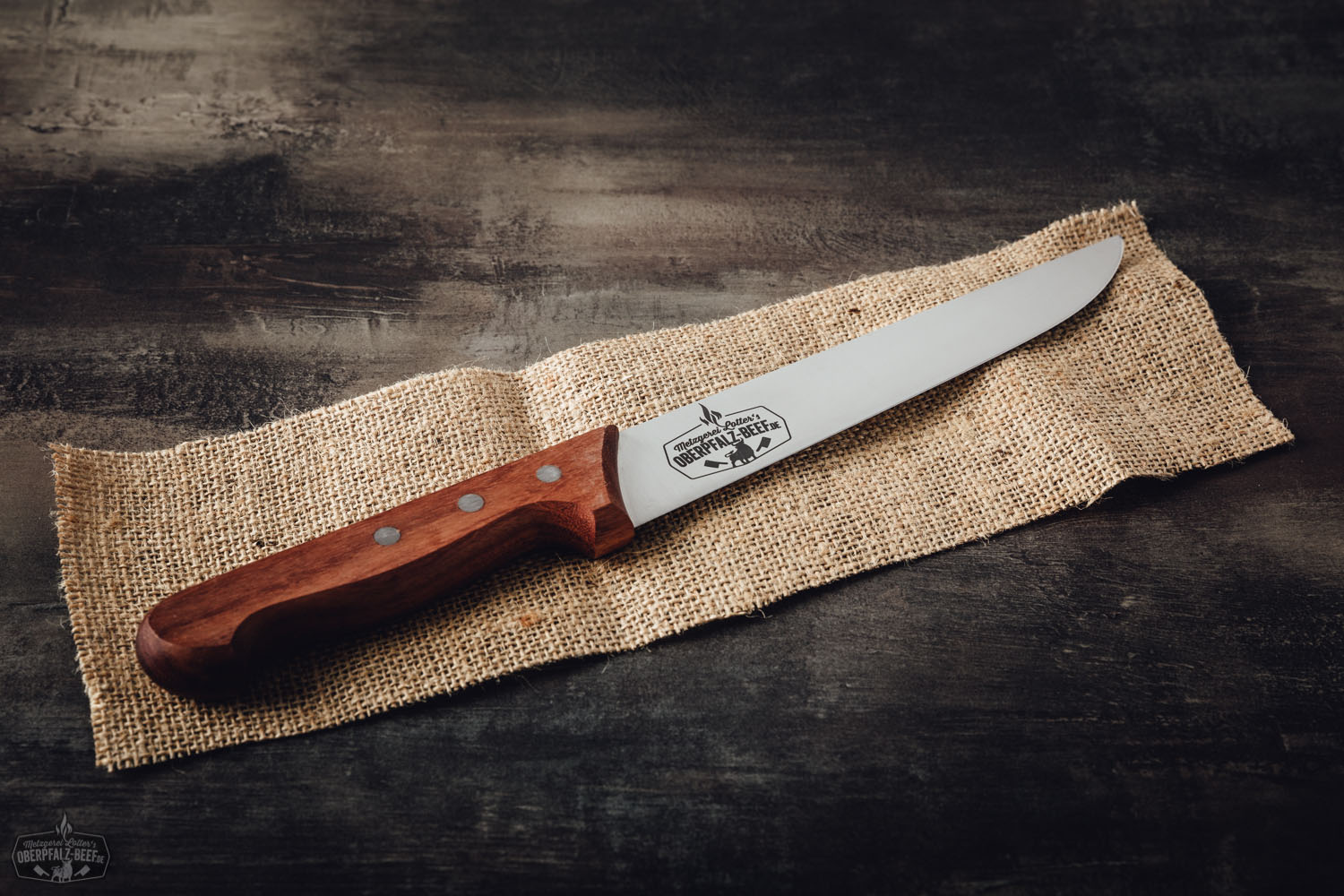 Dick Blockmesser mit Holzgriff im Oberpfalz-Beef-Design, liegend auf dunkler Oberfläche mit sichtbarer Stahlklinge und markantem Logo graviert – ideal für präzises Schneiden von hochwertigem Fleisch.