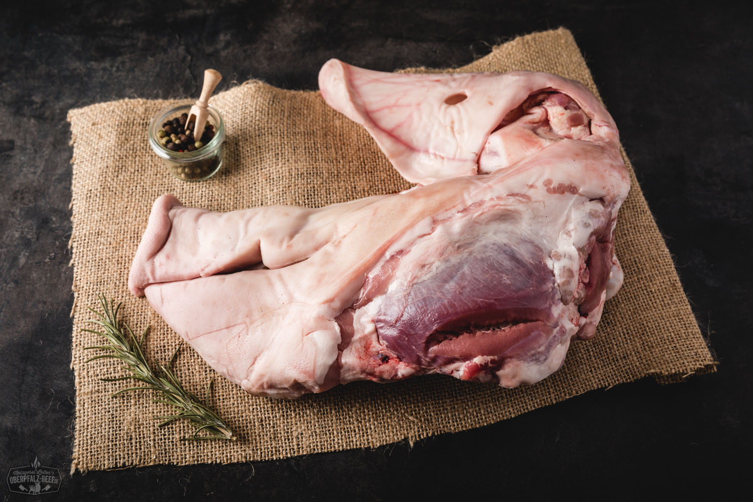 Frischer halber Schweinekopf vom Oberpfälzer Landschwein auf dunklem Untergrund, roh und sauber zugeschnitten, Fleischstruktur und Haut deutlich erkennbar – regionale Fleischspezialität für traditionelle Zubereitungen.