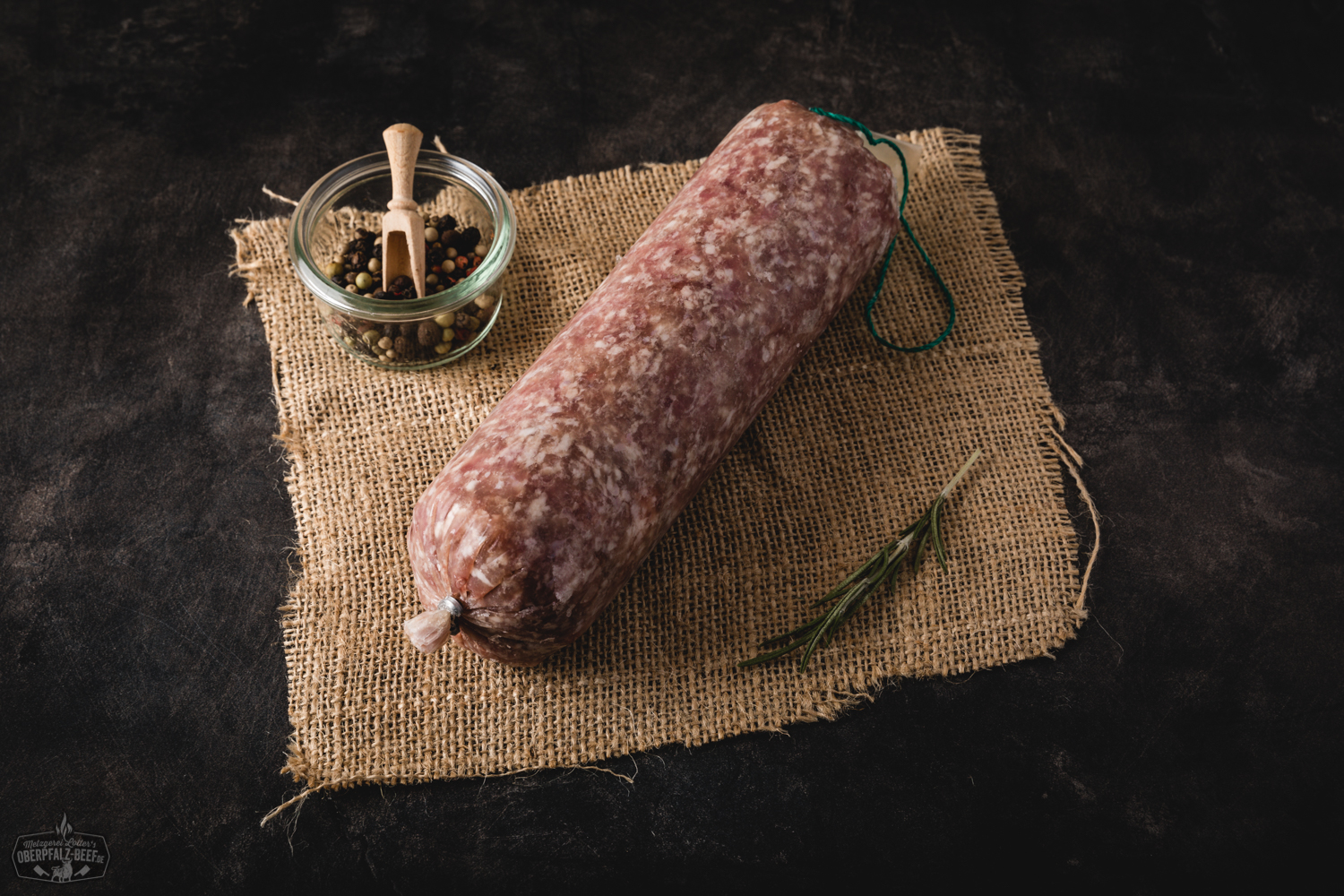 Frisches, rohes Schweinehackfleisch in lockerer Struktur auf einem dunklen Untergrund angerichtet, umgeben von Zutaten wie Knoblauch, roten Zwiebeln, Rosmarin, Salz und Pfeffer – ideale Basis für herzhafte Gerichte mit Schweinefleisch.