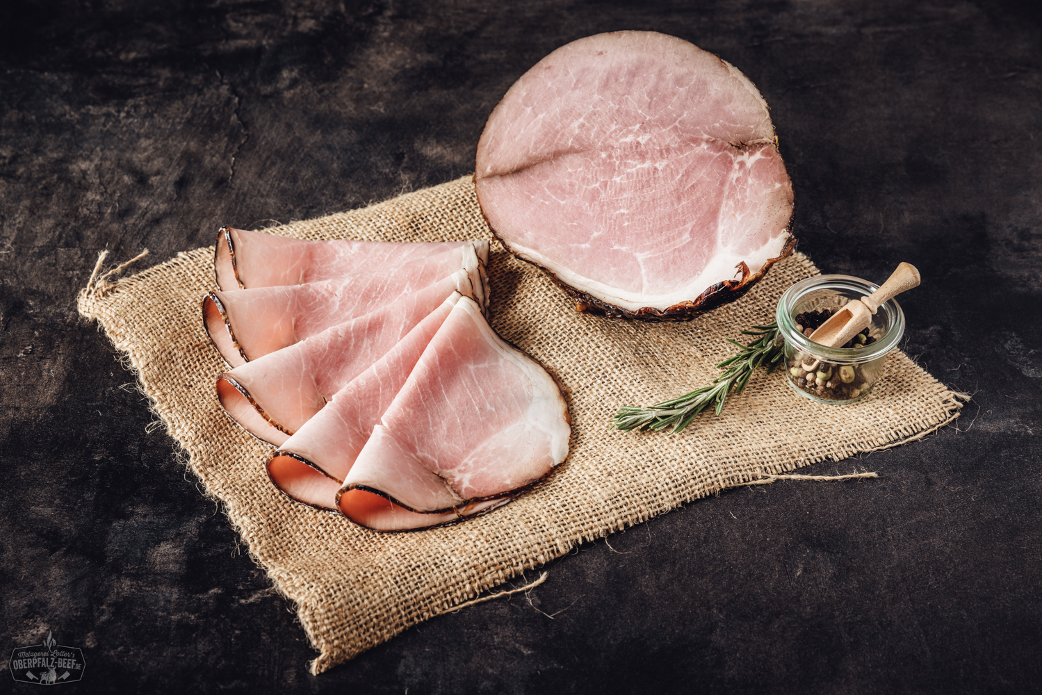 Geschnittener Chilischinken auf dunklem Untergrund, angerichtet mit frischer Petersilie und Chili – feine, rote Schinkenscheiben mit sichtbaren Pfeffer- und Chilistücken, delikat präsentiert für Genießer von pikantem Aufschnitt.