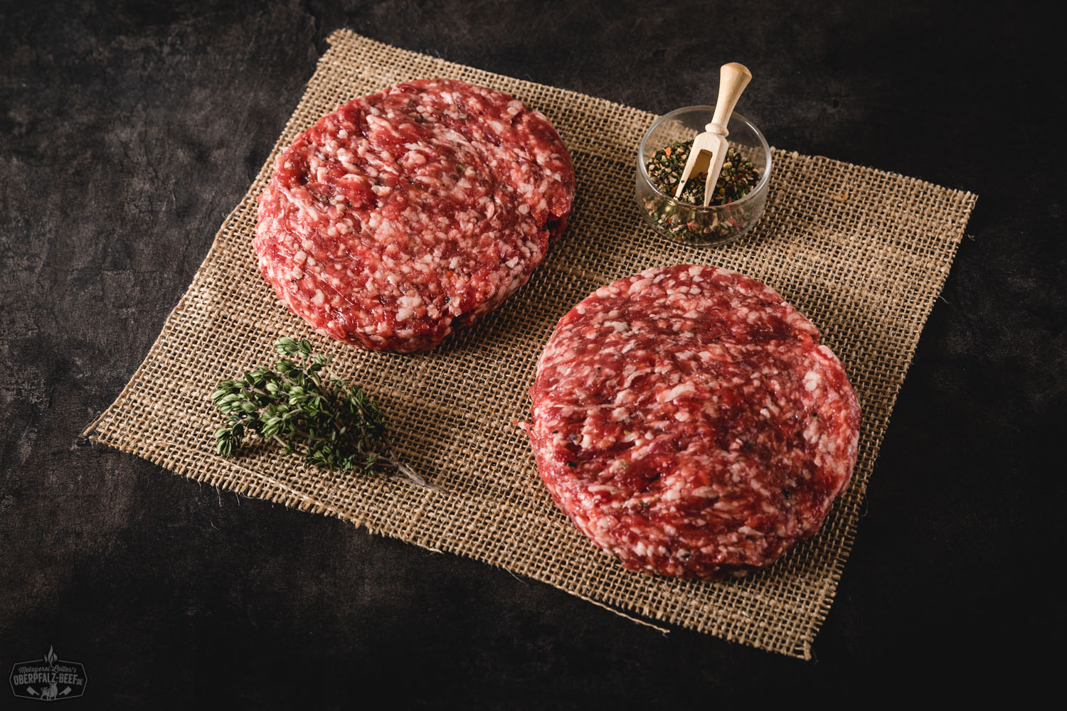 Saftiger Wildburger mit regionalem Wildfleisch auf rustikalem Holzbrett Saftiger Wildburger mit rosa gebratenem Wildfleisch-Patty, knackigem Salat, Tomatenscheiben, roten Zwiebeln und cremiger Sauce in einem rustikalen Sesam-Brioche-Bun, serviert auf Holzbrett mit herbstlicher Dekoration im Hintergrund.