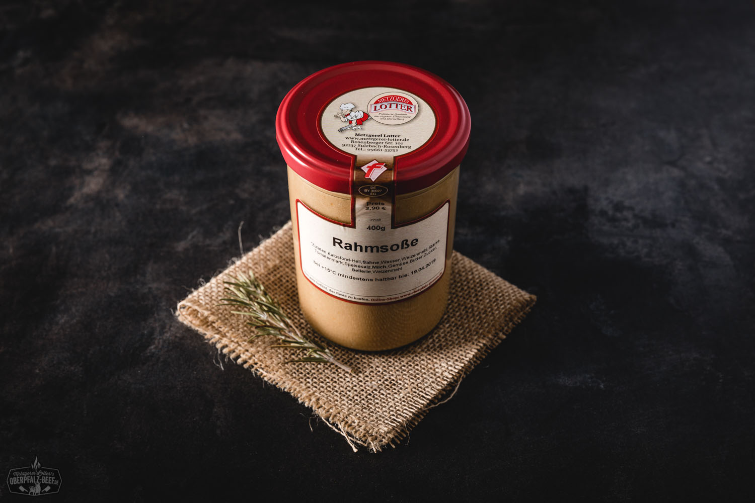 Glas mit cremiger Rahmsoße auf Holzunterlage, daneben frische Zutaten wie Pfeffer, Zwiebeln und Kräuter – hochwertige hausgemachte Sauce im Einmachglas für Fleischgerichte.