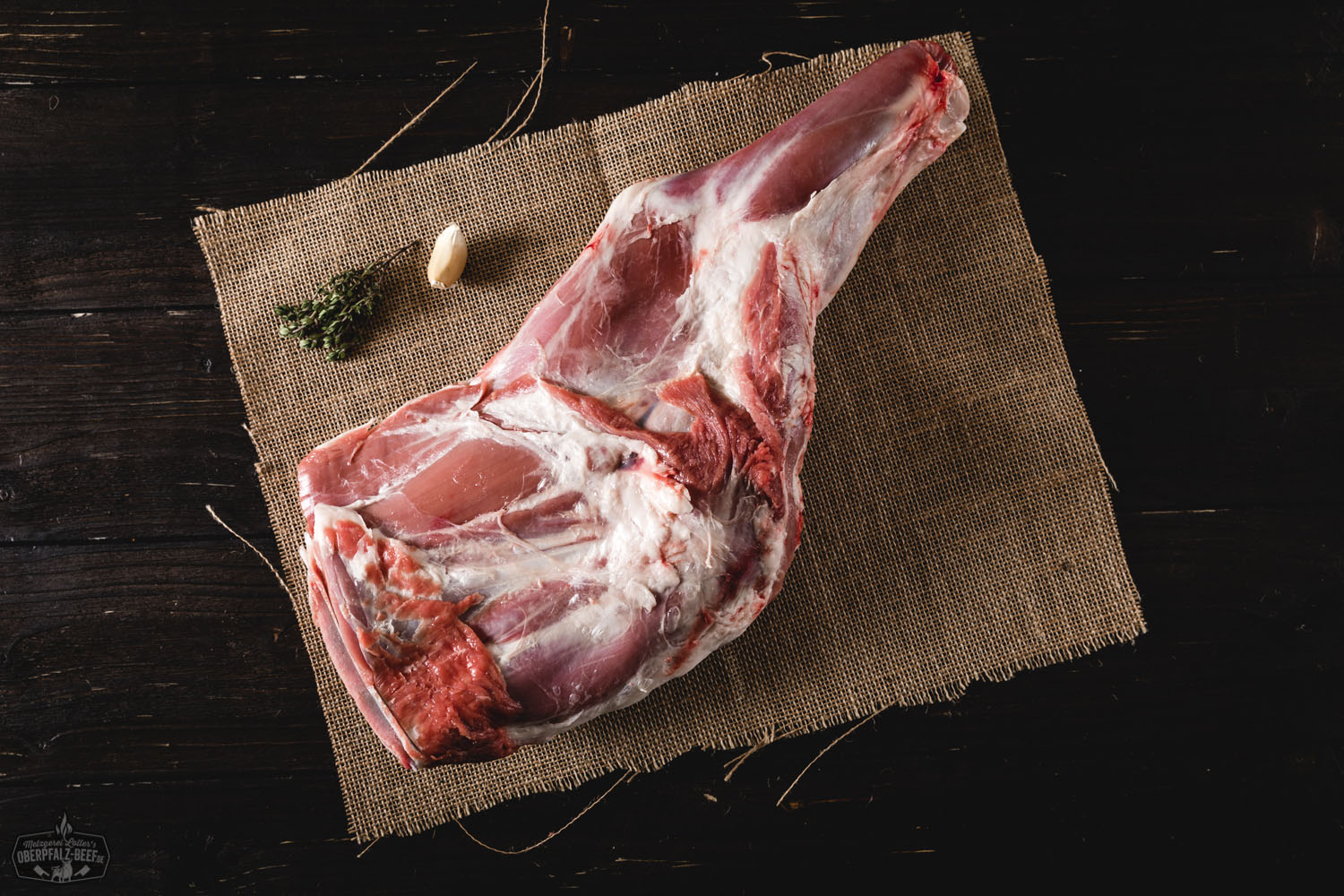 Lammschulter mit Knochen vom Juradistl-Lamm – Regionales Weidefleisch aus der Oberpfalz Rohe Lammschulter mit Knochen vom Juradistl-Lamm, saftig marmoriert und auf einem dunklen Untergrund angerichtet, umgeben von Rosmarinzweigen, Knoblauch und Gewürzen – ideale Fleischzuschnitt für Braten oder Schmorgerichte in nachhaltiger Bio-Qualität.