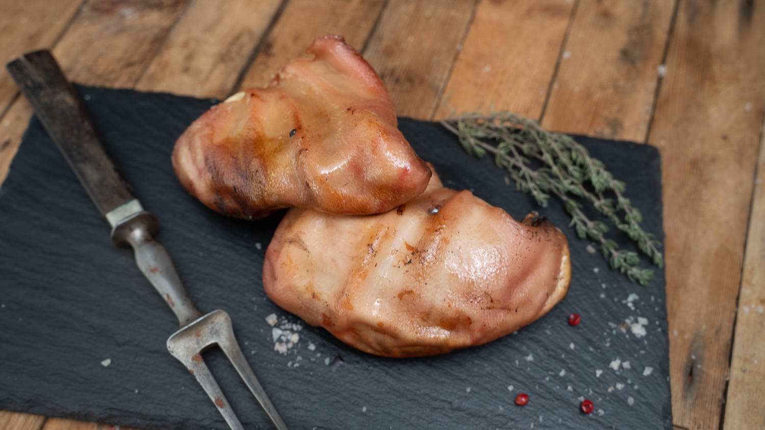 Ohren vom Oberpfälzer Landschwein – Regionales Schweinefleisch direkt vom Erzeuger Roh geschnittene Schweineohren vom Oberpfälzer Landschwein liegen appetitlich auf einem dunklen Holzbrett, umgeben von grobem Salz, Pfeffer und frischen Kräutern – hochwertige regionale Fleischspezialität aus Bayern.