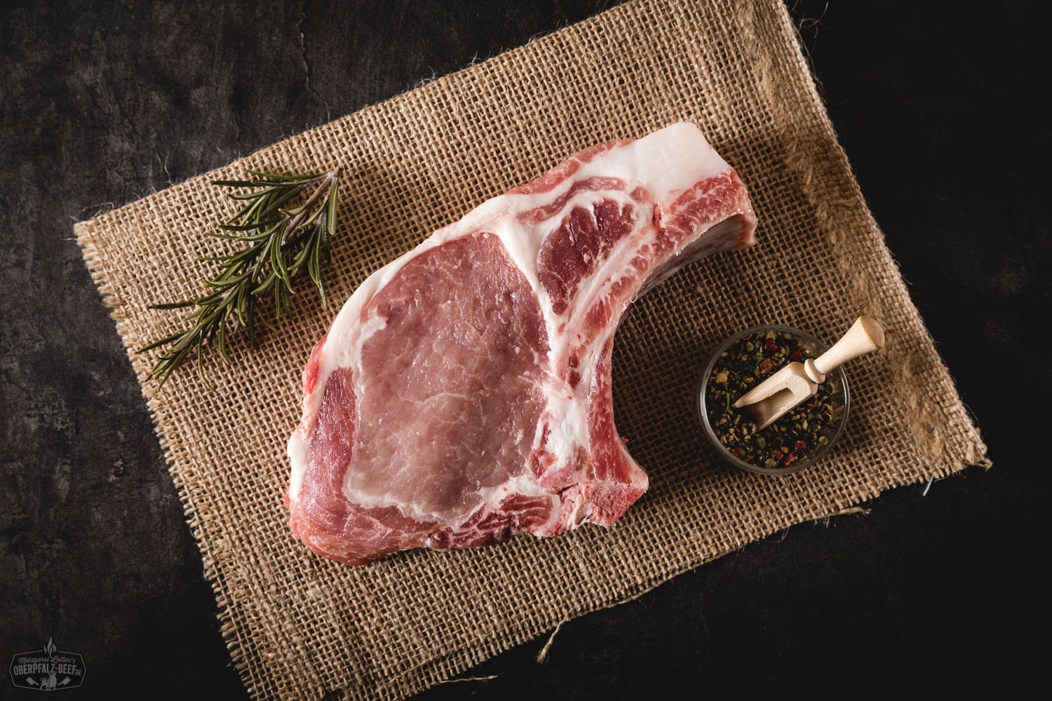 Metzgerkotelett vom Oberpfälzer Landschwein – Regionales Qualitätsfleisch direkt vom Erzeuger Rohes Metzgerkotelett vom Oberpfälzer Landschwein mit sichtbarem Knochen, marmoriertem Fleisch und feiner Fettauflage, auf dunklem Untergrund angerichtet – ideale Fleischqualität für Grill oder Pfanne.