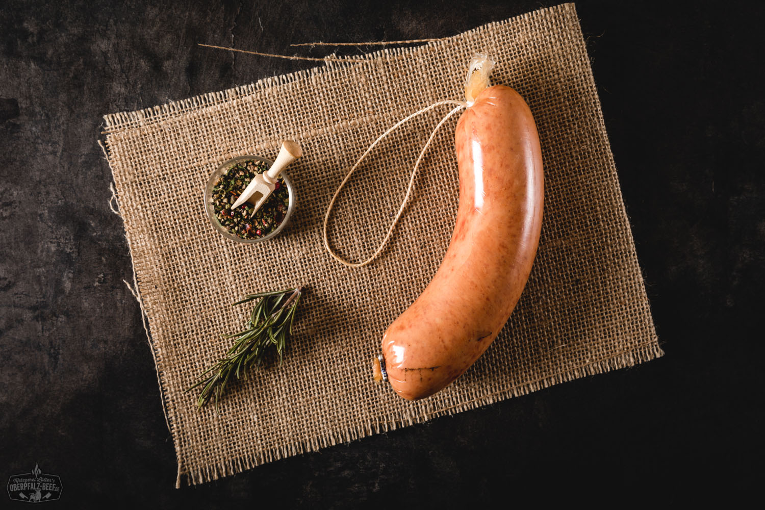 Mittelgrobe Mettwurst in Scheiben geschnitten auf einem rustikalen Holzbrett, angerichtet mit frischen Kräutern und einer Brotscheibe im Hintergrund – typisch deutsche Wurst-Spezialität aus der Oberpfalz, ideal für Brotzeit oder kalte Platten.