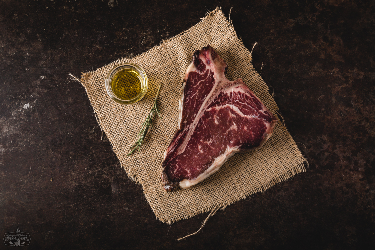 Dry Aged T-Bone Steak vom Oberpfälzer Milchkalb – Premium Fleischqualität Dry Aged T-Bone-Steak vom oberpfälzer Milchkalb auf dunklem Untergrund, roh, marmoriert mit sichtbarem Knochen, hochwertige Fleischstruktur, rustikal präsentiert für Gourmet-Grillen und Fleischliebhaber.