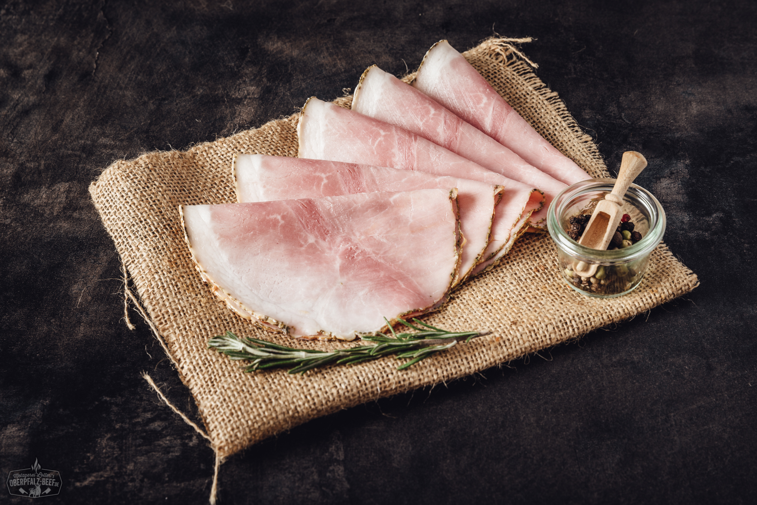 Geschnittener Rosmarinschinken auf Holzbrett – hochwertiger Aufschnitt mit frischen Kräutern Aufgeschnittener Rinderschinken im cremigen Meerrettichmantel, angerichtet auf dunkler Schieferplatte, mit Petersiliengarnitur – delikate Feinkost-Spezialität aus der Oberpfalz.