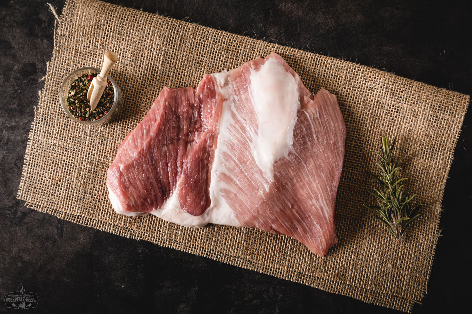 Secreto vom Oberpfälzer Landschwein, roh und saftig marmoriert, sorgfältig auf einem dunklen Holzbrett angerichtet, daneben frische Kräuter und grobes Meersalz – ein hochwertiges regionales Fleischstück für Grill oder Pfanne.