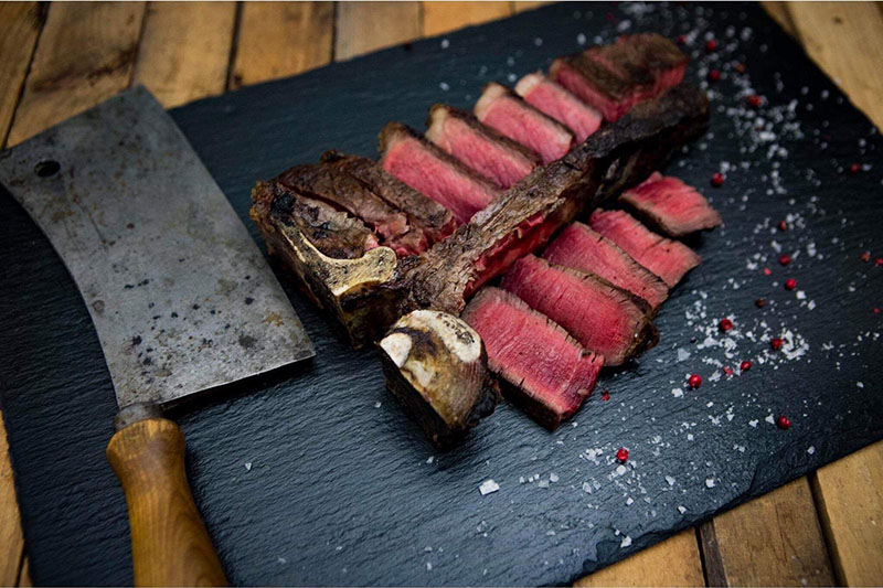 Dry Aged T-Bone Steak vom Oberpfalz-Rind – Premium Rindfleisch aus Bayern Auf einem Holzbrett liegt ein Stück zart marmoriertes Kalbfleisch, die Nuss vom Oberpfälzer Milchkalb, roh und frisch zugeschnitten; daneben frische Rosmarinzweige, Pfefferkörner und Meersalz – hochwertige Zutaten für Feinschmecker und Fleischliebhaber.