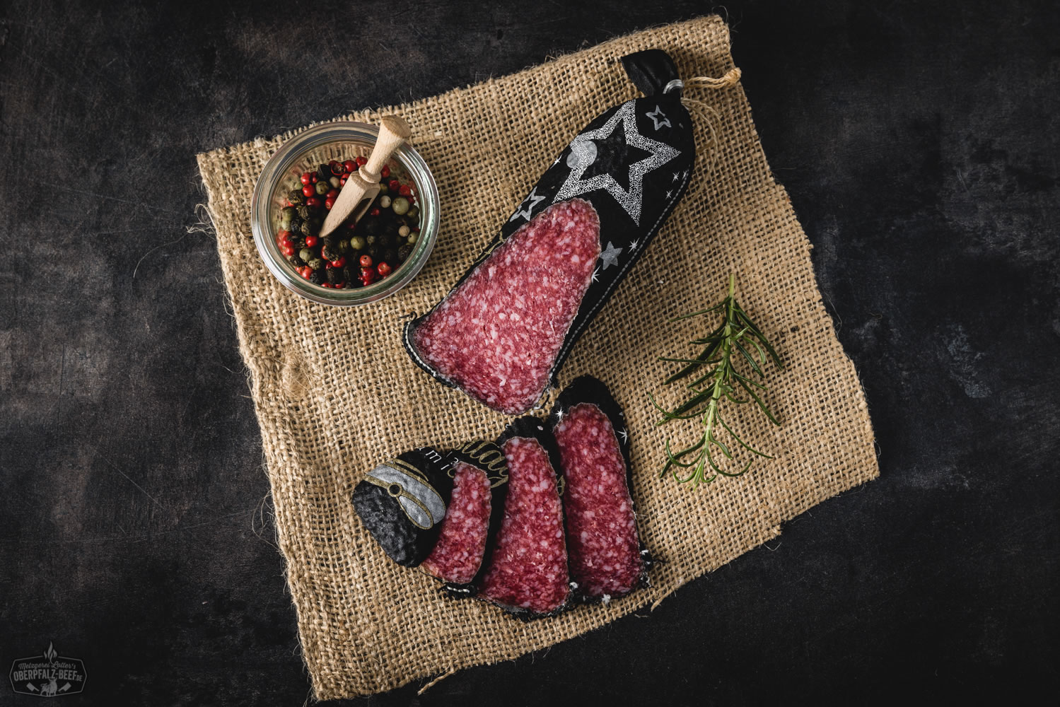 Festtagssalami aus 100 % regionalem Rindfleisch – Oberpfalz Beef Delikatesse Festtagssalami im Anschnitt auf Holzbrett angerichtet, dekoriert mit Rosmarinzweig und Pfefferkörnern – traditionelle Delikatesswurst aus der Oberpfalz, ideal für Festtage und Feinschmecker.